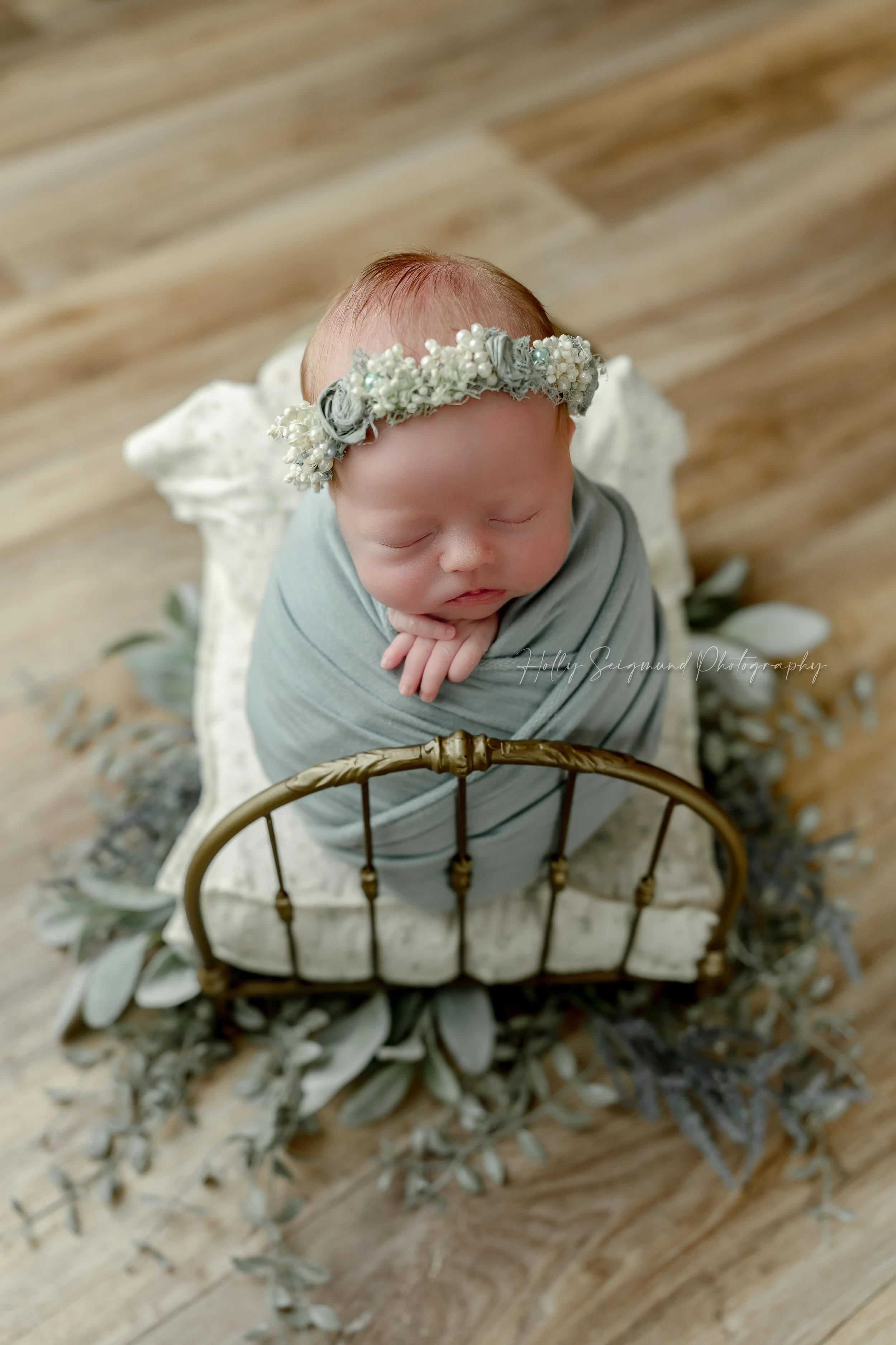 Posed newborn girl in a small brass bed, wrapped in a mint wrap and floral crown in a newborn photography studio in Blue, Texas