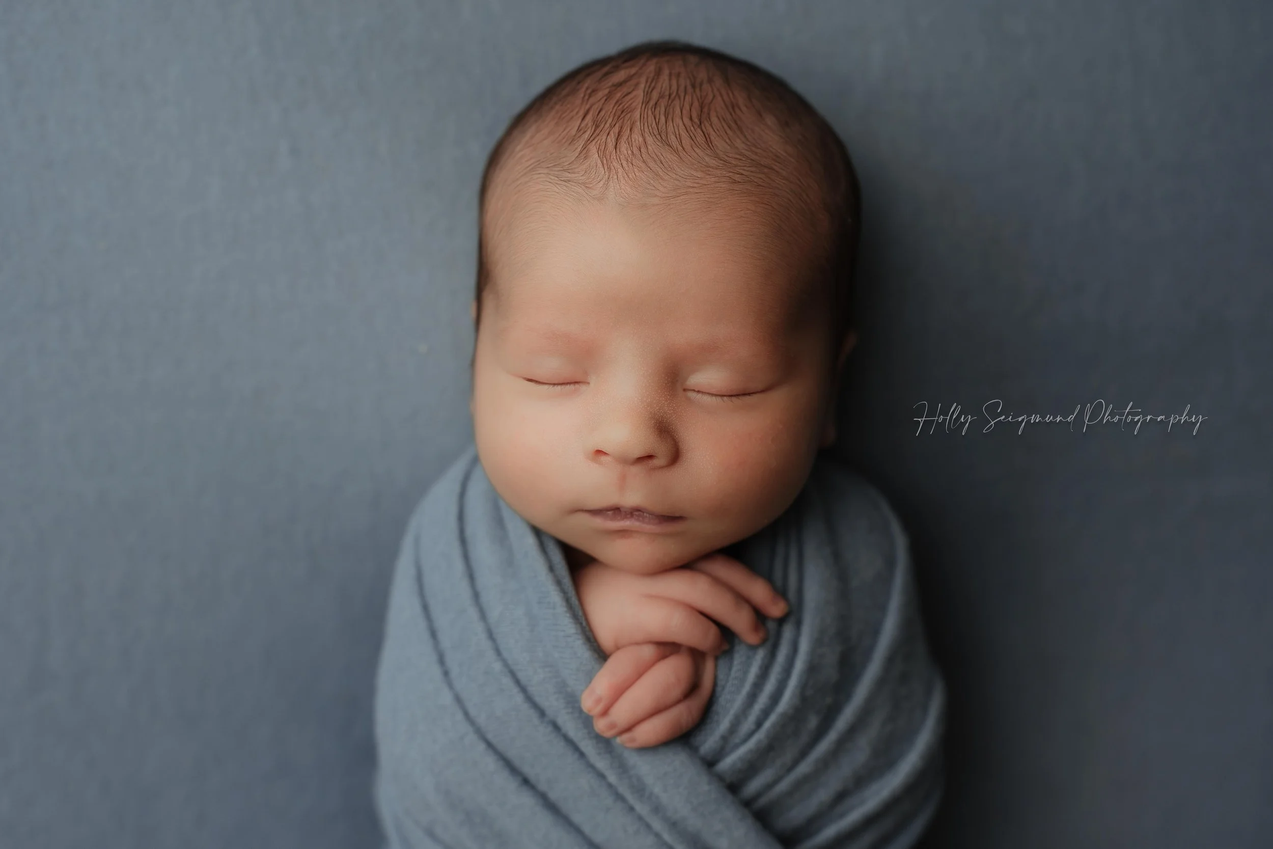 Baby boy wrapped in blue on a light blue backdrop for newborn photos in Elgin, Texas
