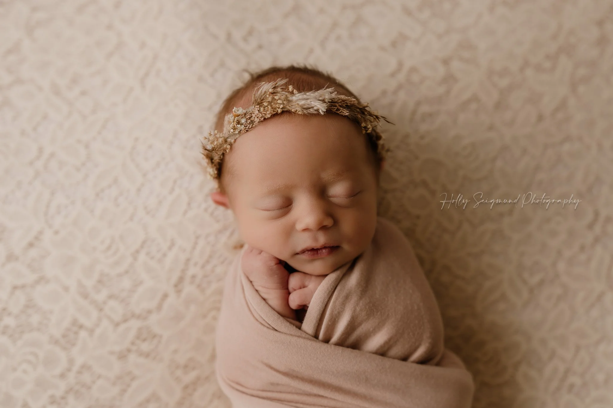Newborn girl with a floral headband on a pink lace backdrop and pink wrap, in-studio in Central Texas