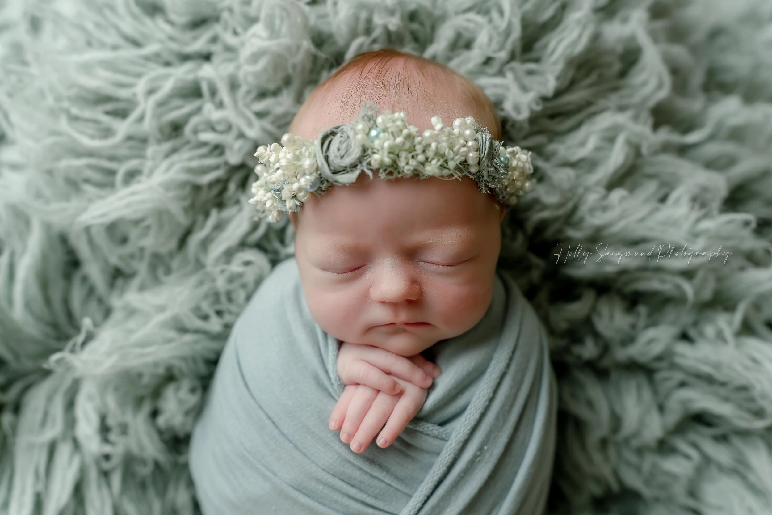 Baby girl with a mint colored wrap, floral crown and fluffy backdrop during a studio newborn session in Lexington, Texas