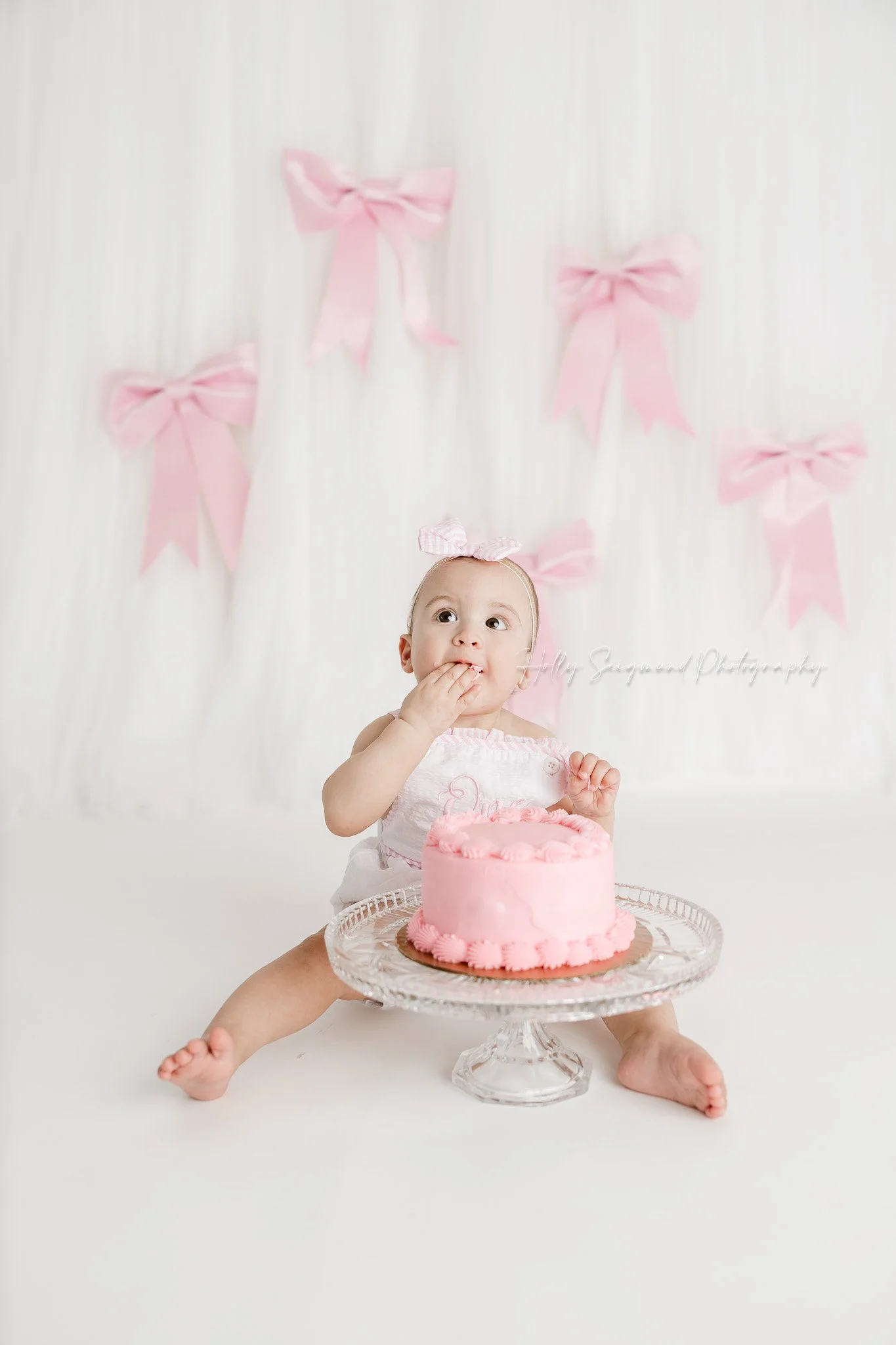 Little girls first birthday smash cake session with pink bows in a flash photography studio in Lexington Texas
