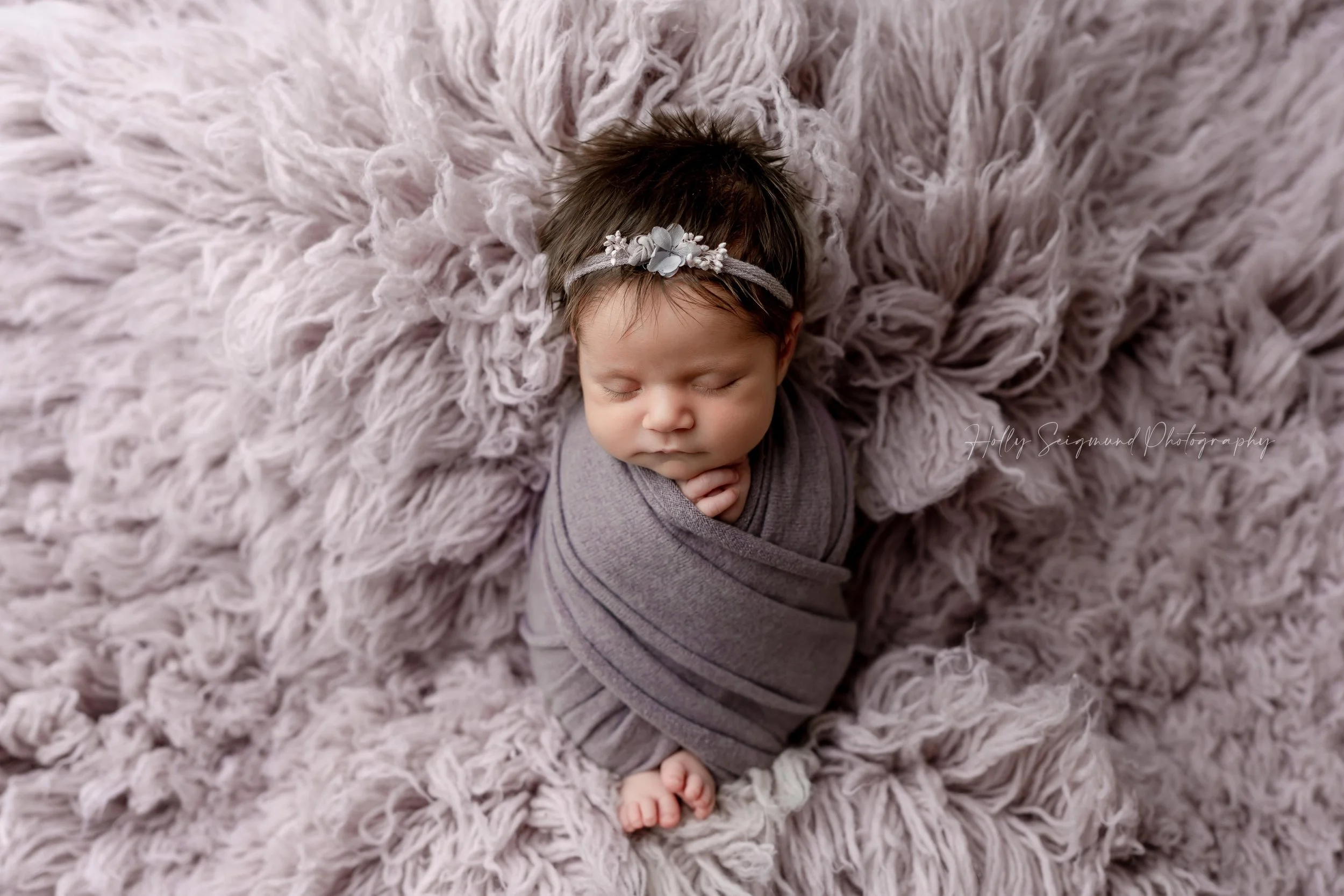 Baby girl with lots of dark hair, wrapped and posed in light purple during a studio newborn session in Lexington, Texas