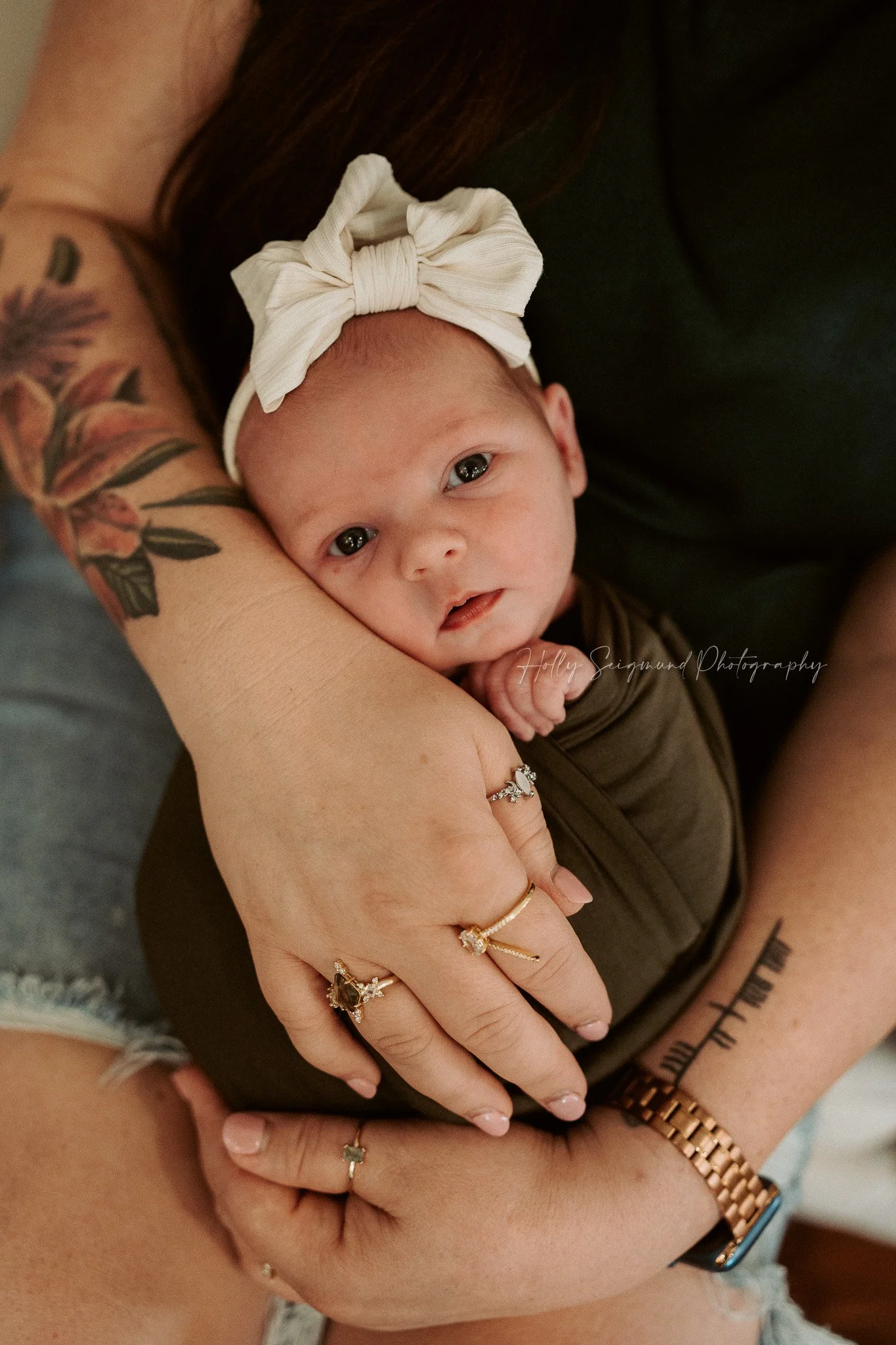 Mom's tattooed arms wrapped around her newborn baby girl during an in-home moody toned lifestyle newborn session