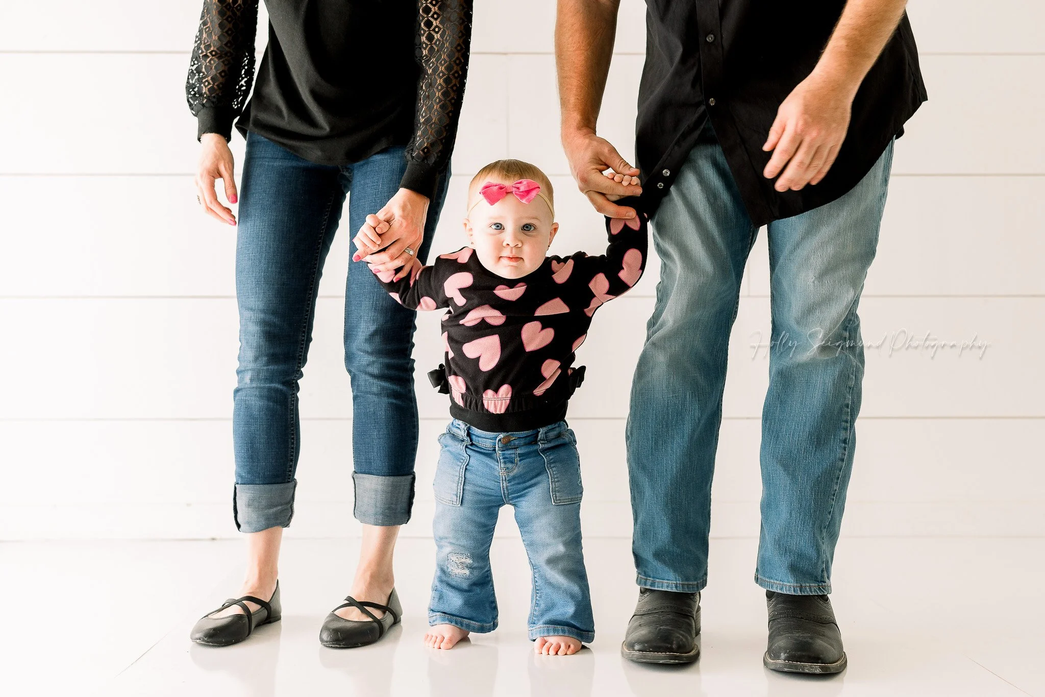 First birthday girl holding mom and dad's hands in a natural light studio in Lexington, Texas