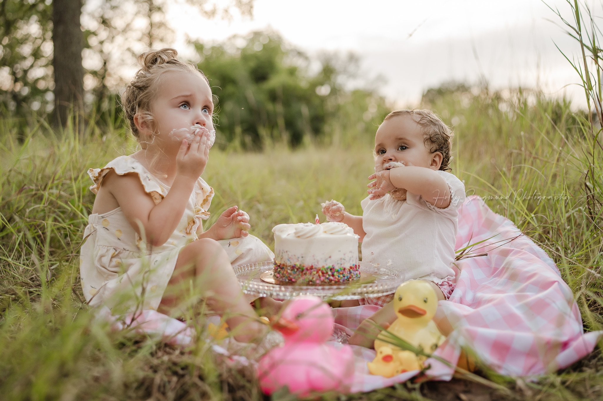 Sisters sharing cake for a first birthday in the grass in Lee County Texas