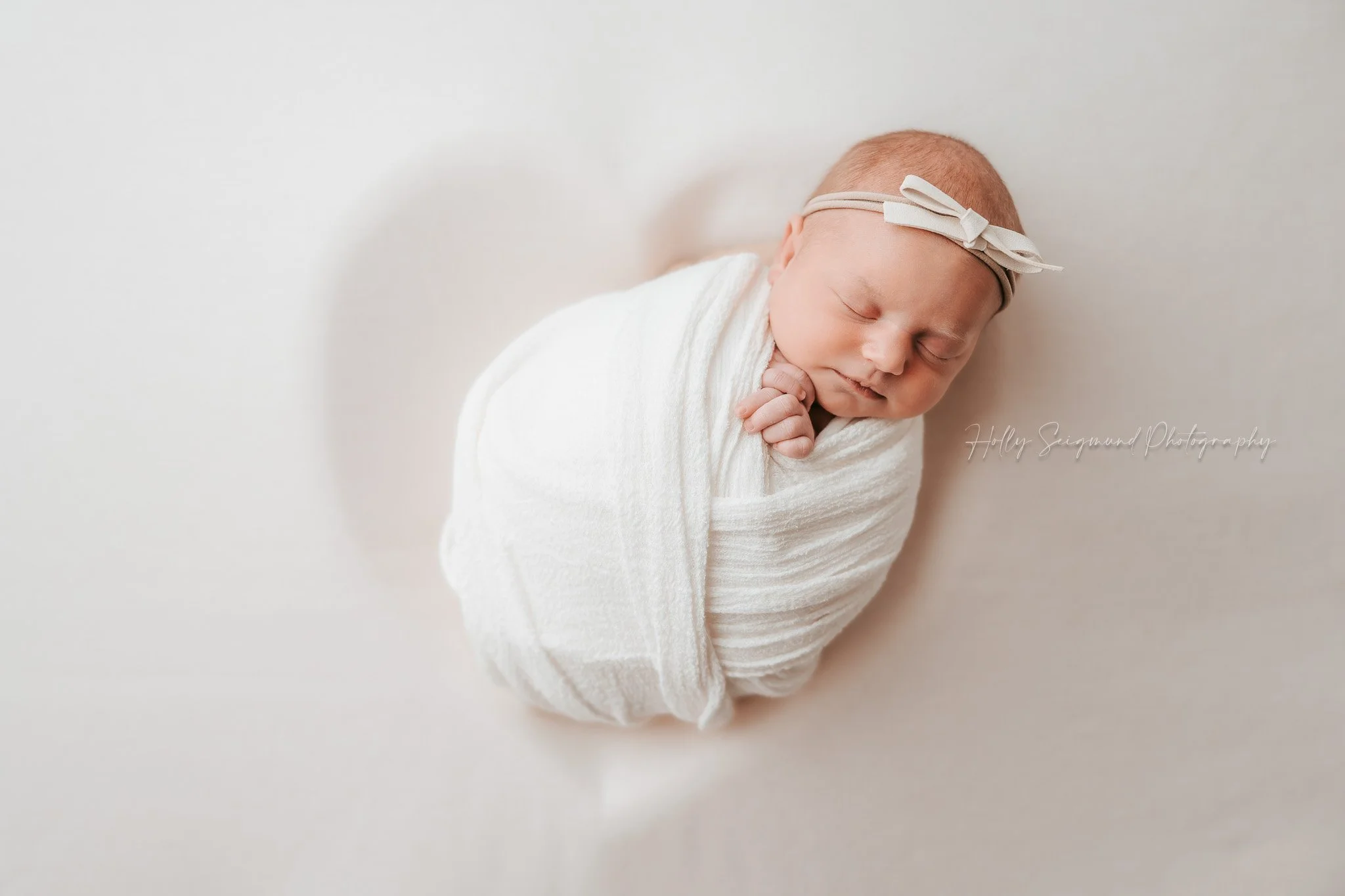 Central Texas Newborn on white heart backdrop with white wrap and bow