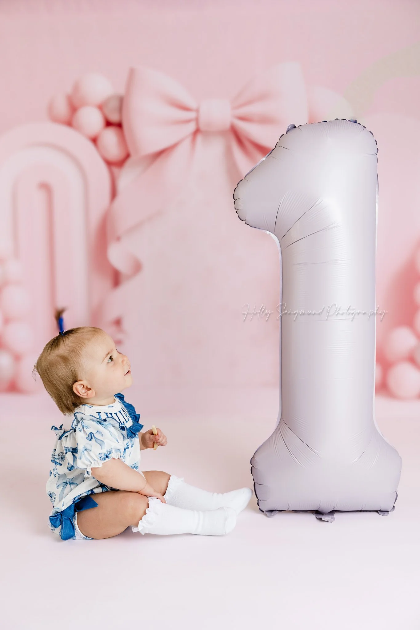 In studio session in Lexington, Texas for a girls first birthday session with pink bow backdrop and number 1 balloon