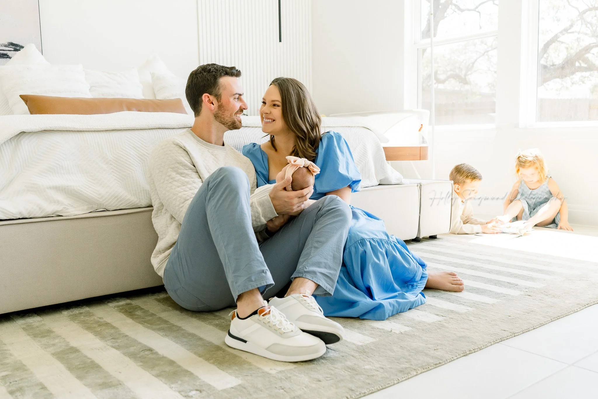 Mom and dad with newborn and siblings playing in the background in a lifestyle newborn session in Central Texas