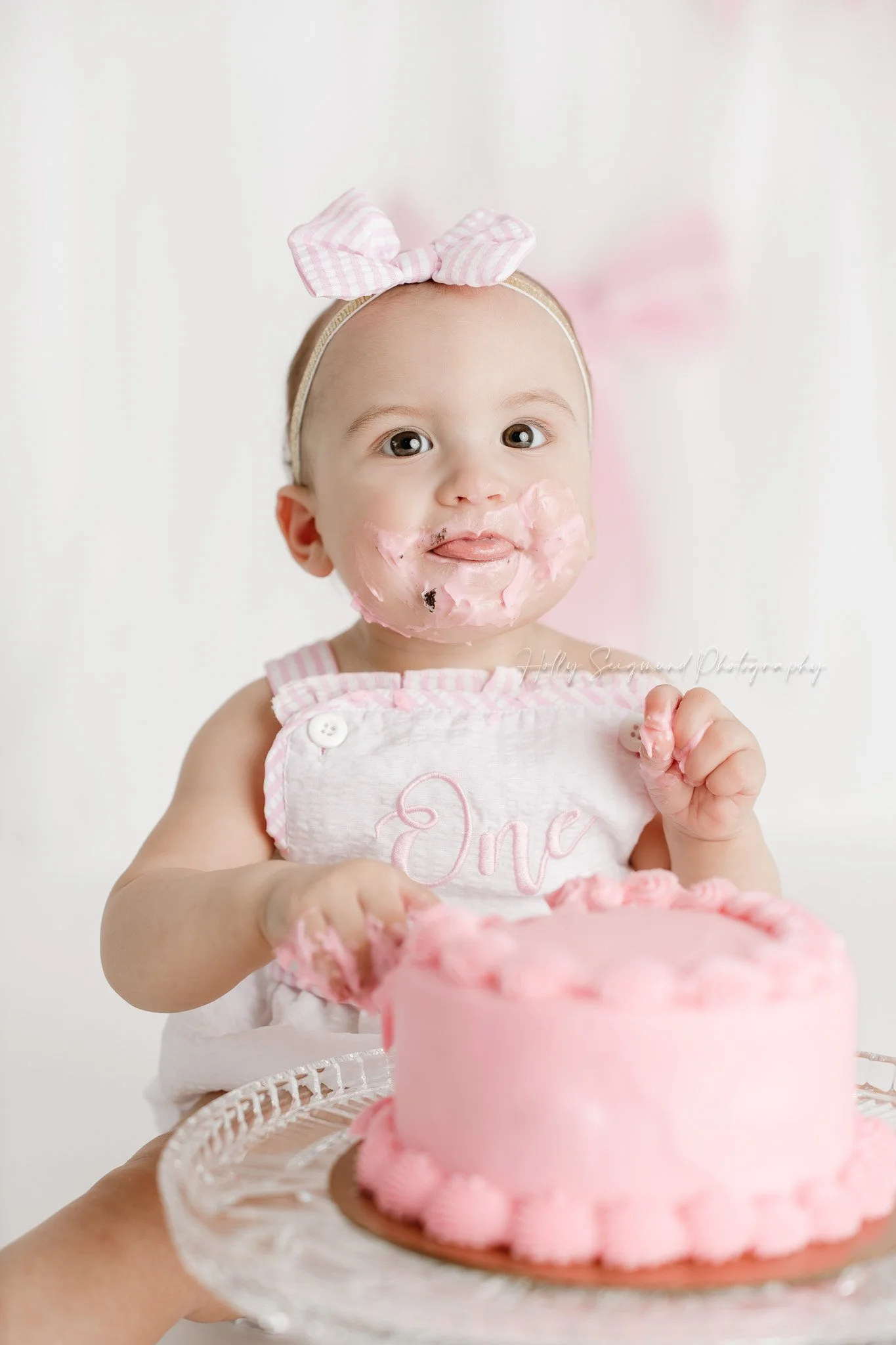 Little girls first birthday smash cake session with pink bows in a flash photography studio in Central Texas