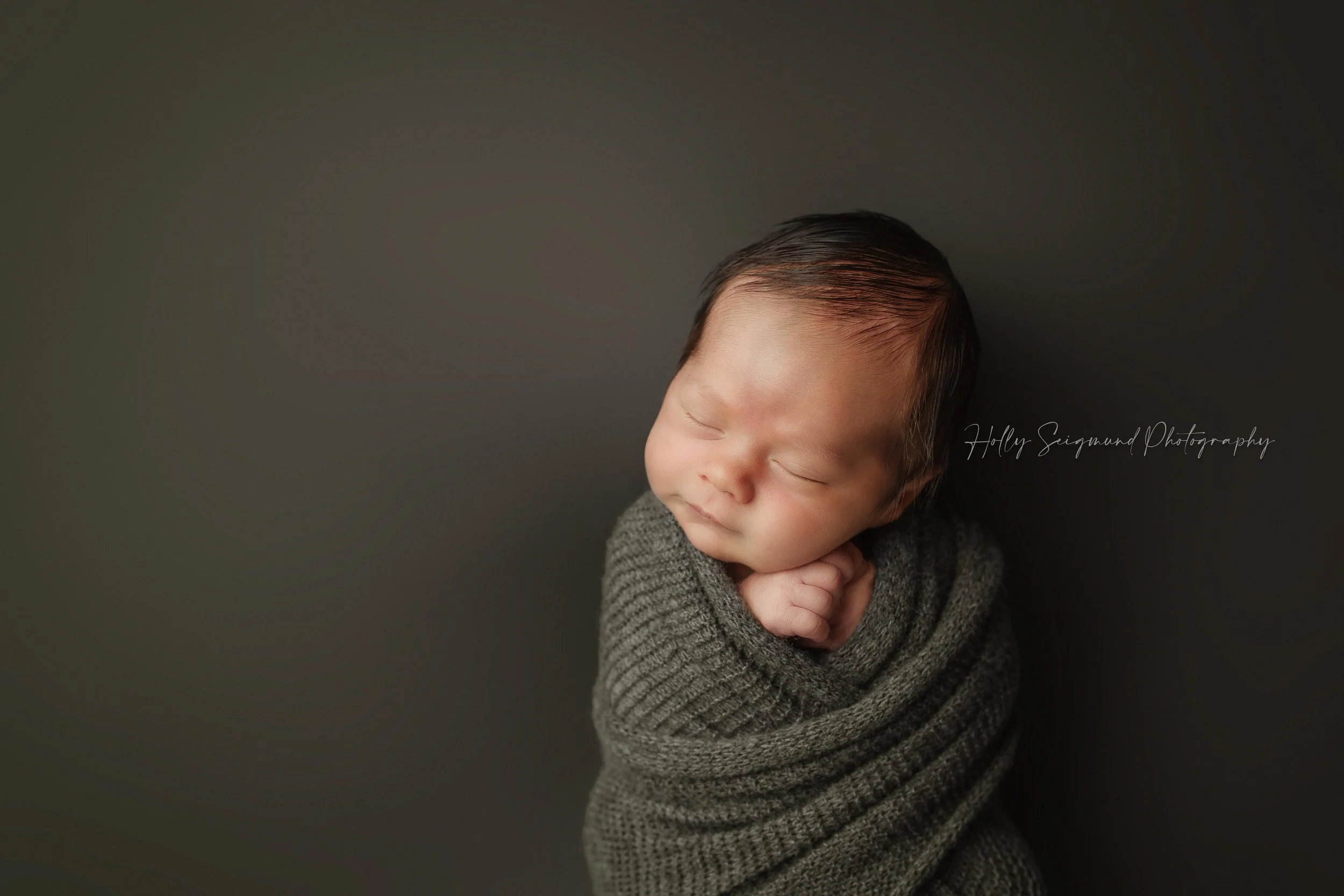 Newborn baby boy wrapped in olive green on a olive green backdrop in a photography studio in Lexington, Texas