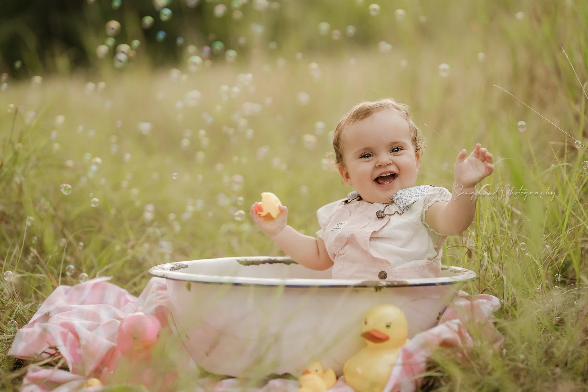 One year old girl in a metal tub sitting in the grass with bubbles in the air