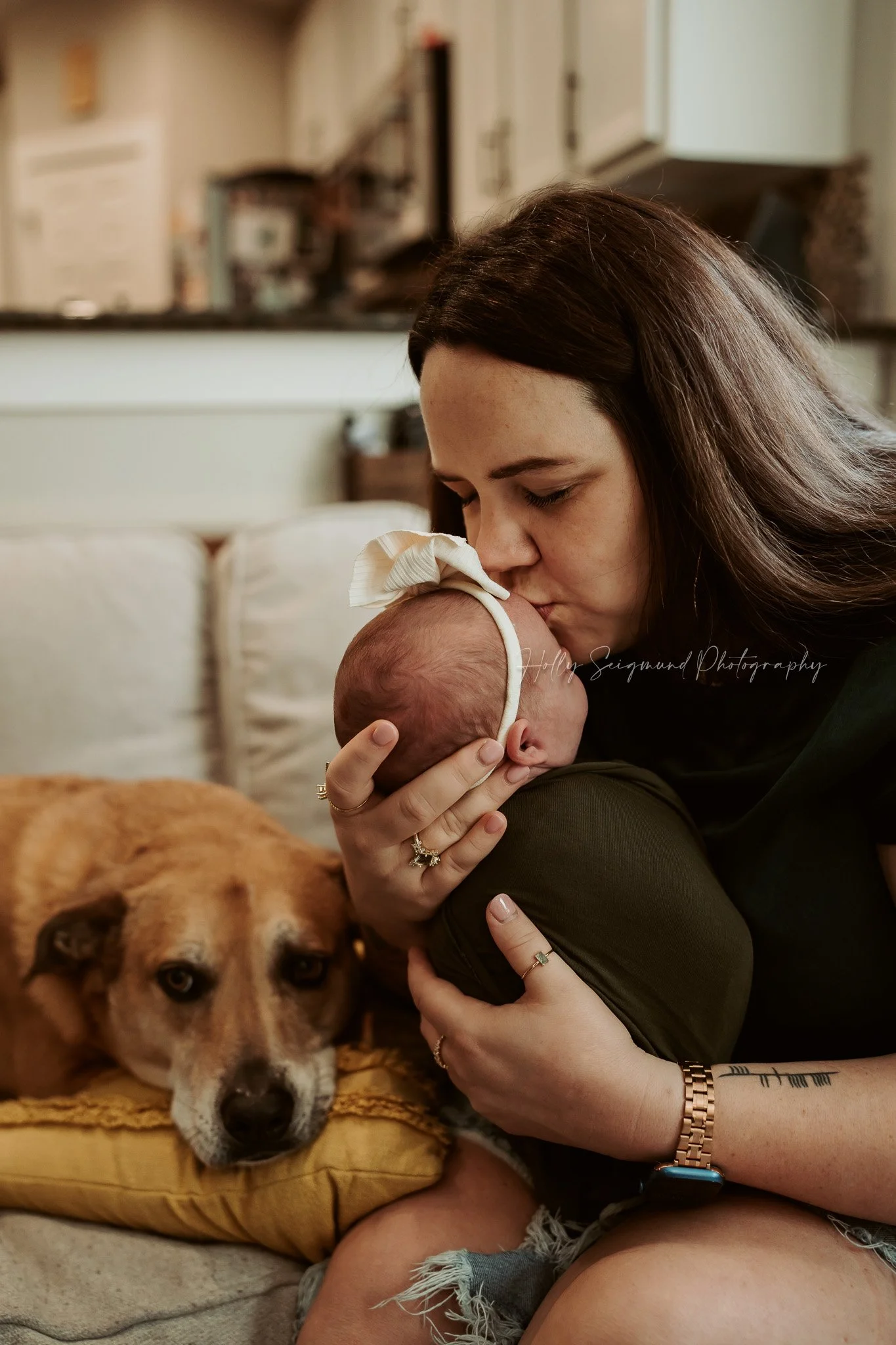 Mom kissing baby with dog on the couch during a lifestyle newborn session in Central Texas