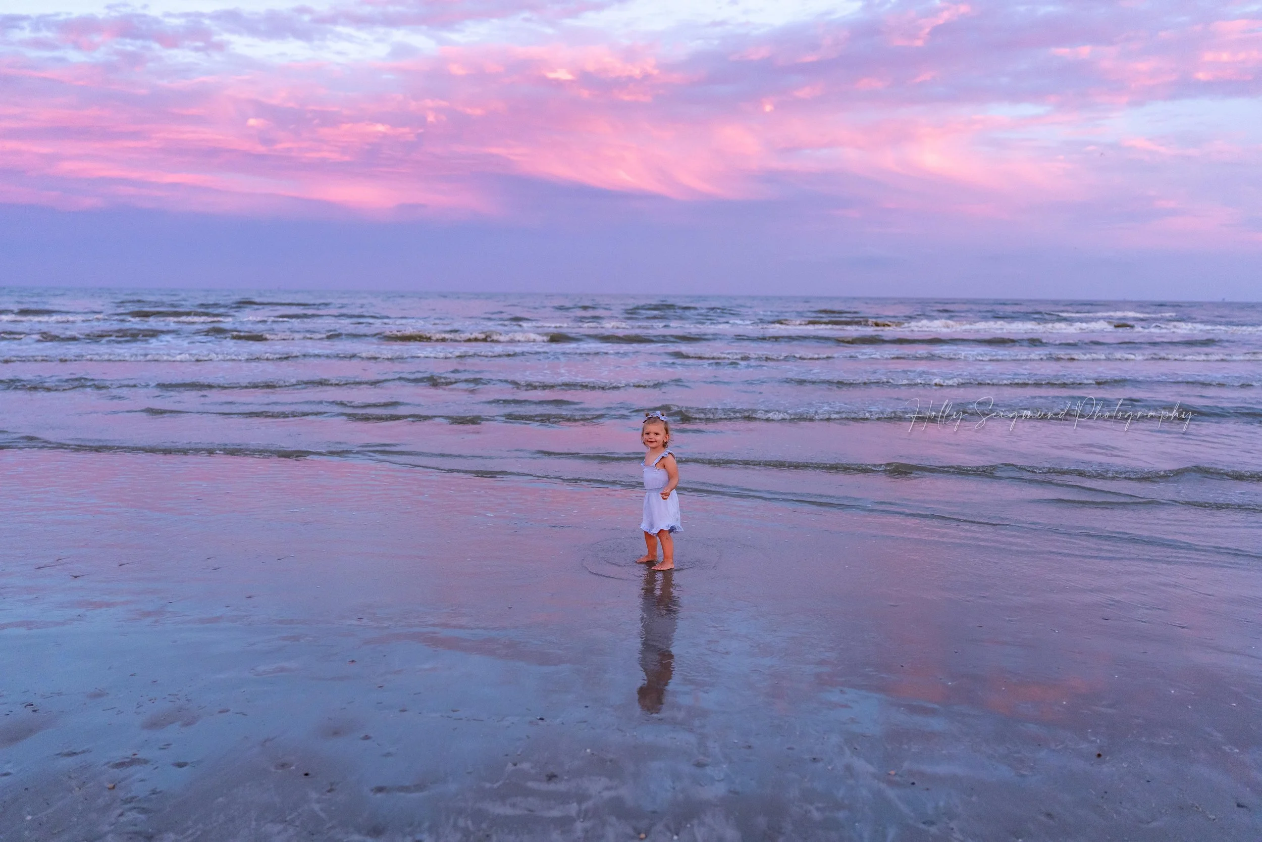 Toddler standing in the waves under a pink and purple sunset in Port Aransas Texas