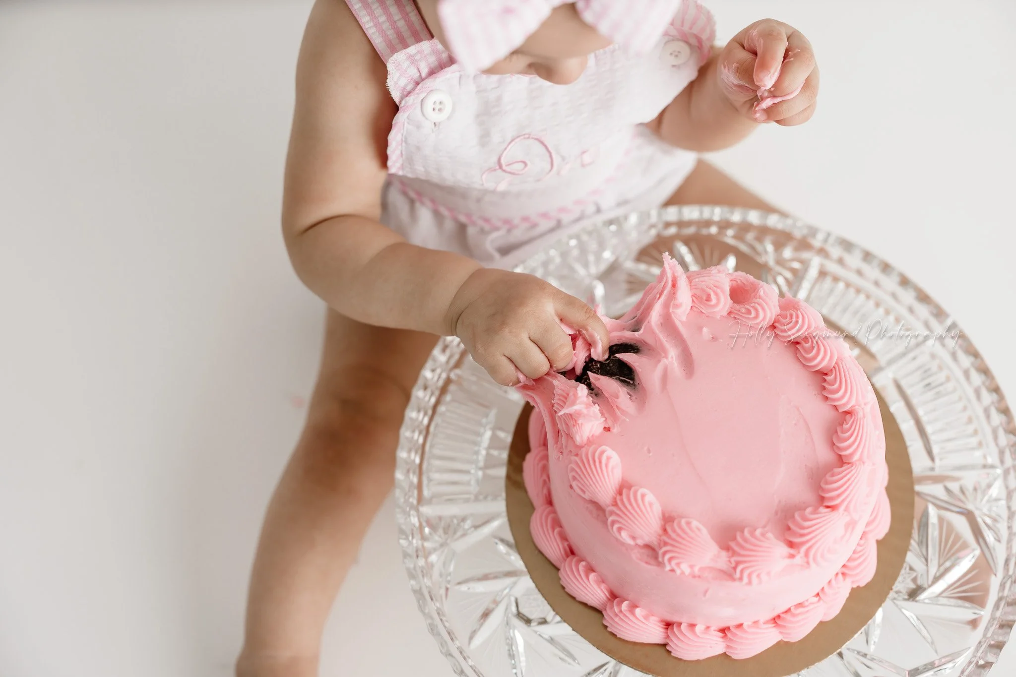Little girls first birthday smash cake session with pink bows in a flash photography studio near Lexington, Texas