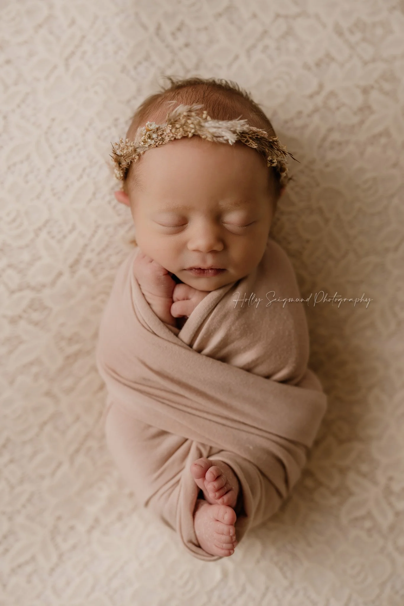 Newborn in a criss-cross pink wrap on a lace backdrop in Central Texas with a floral crown