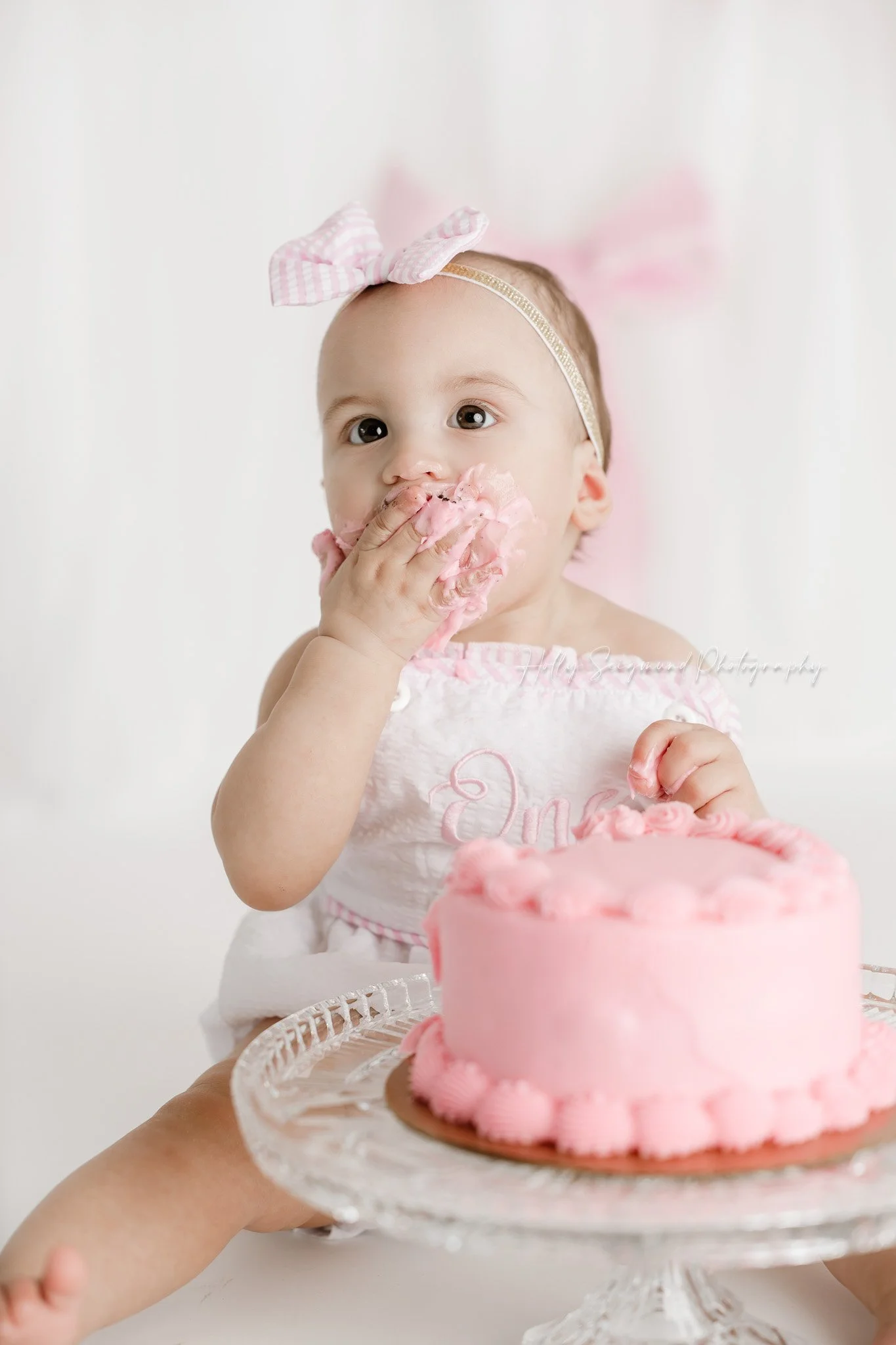 Little girls first birthday smash cake session with pink bows in a flash photography studio in Lee County Texas