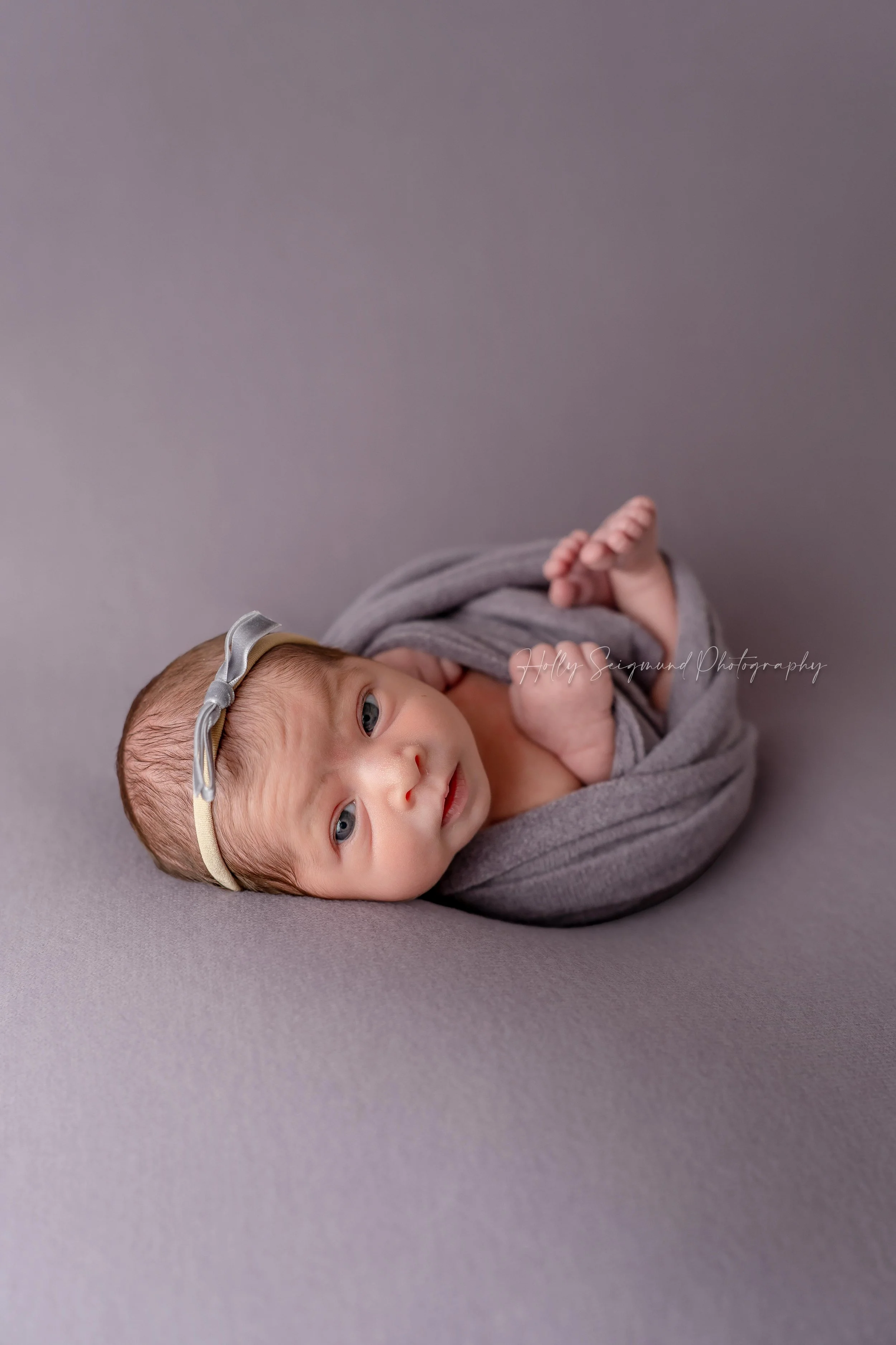 Newborn baby girl wrapped in purple during a studio newborn session in Blue, Texas