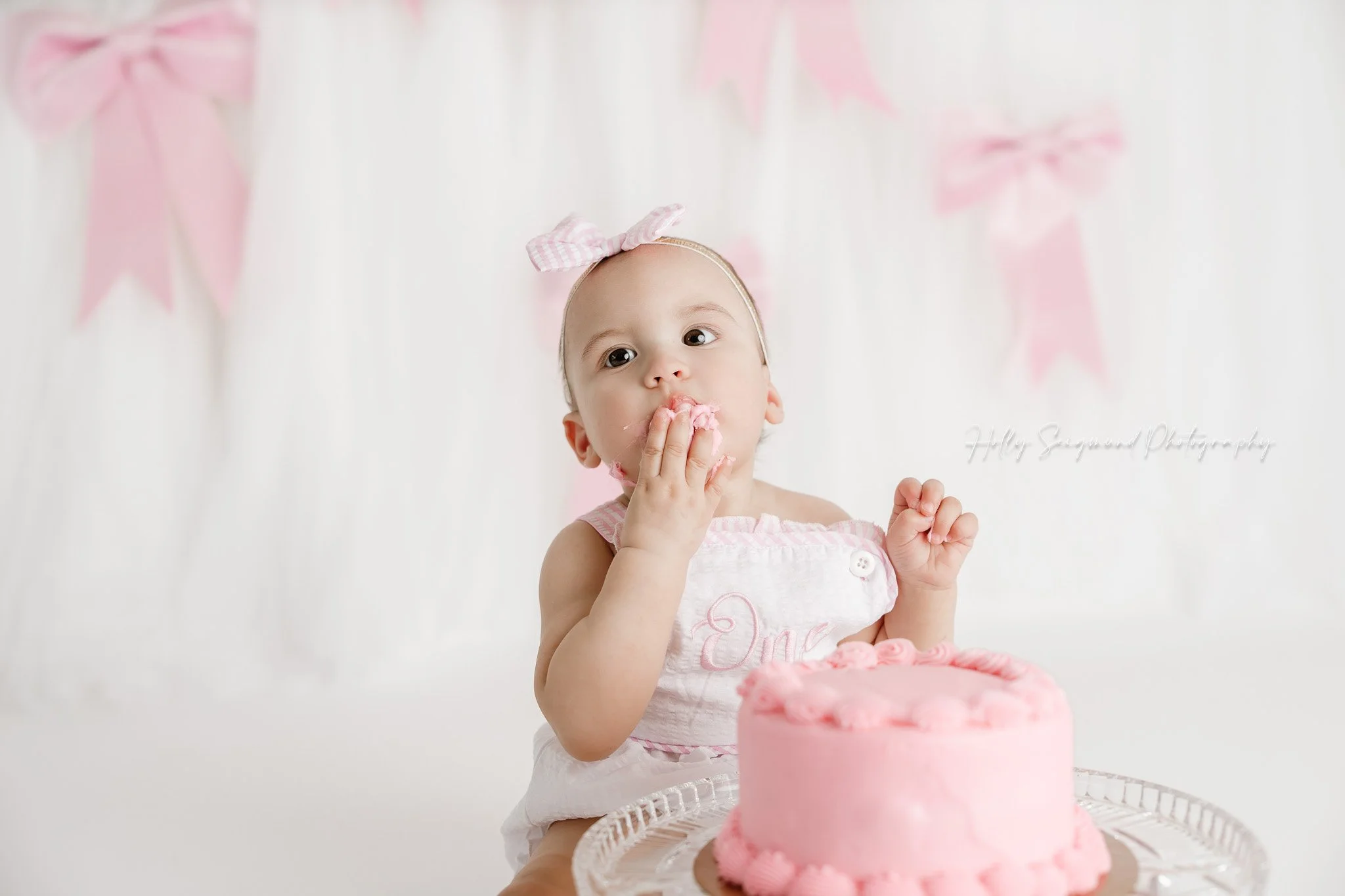 Little girls first birthday smash cake session with pink bows in a flash photography studio in Lee County Texas