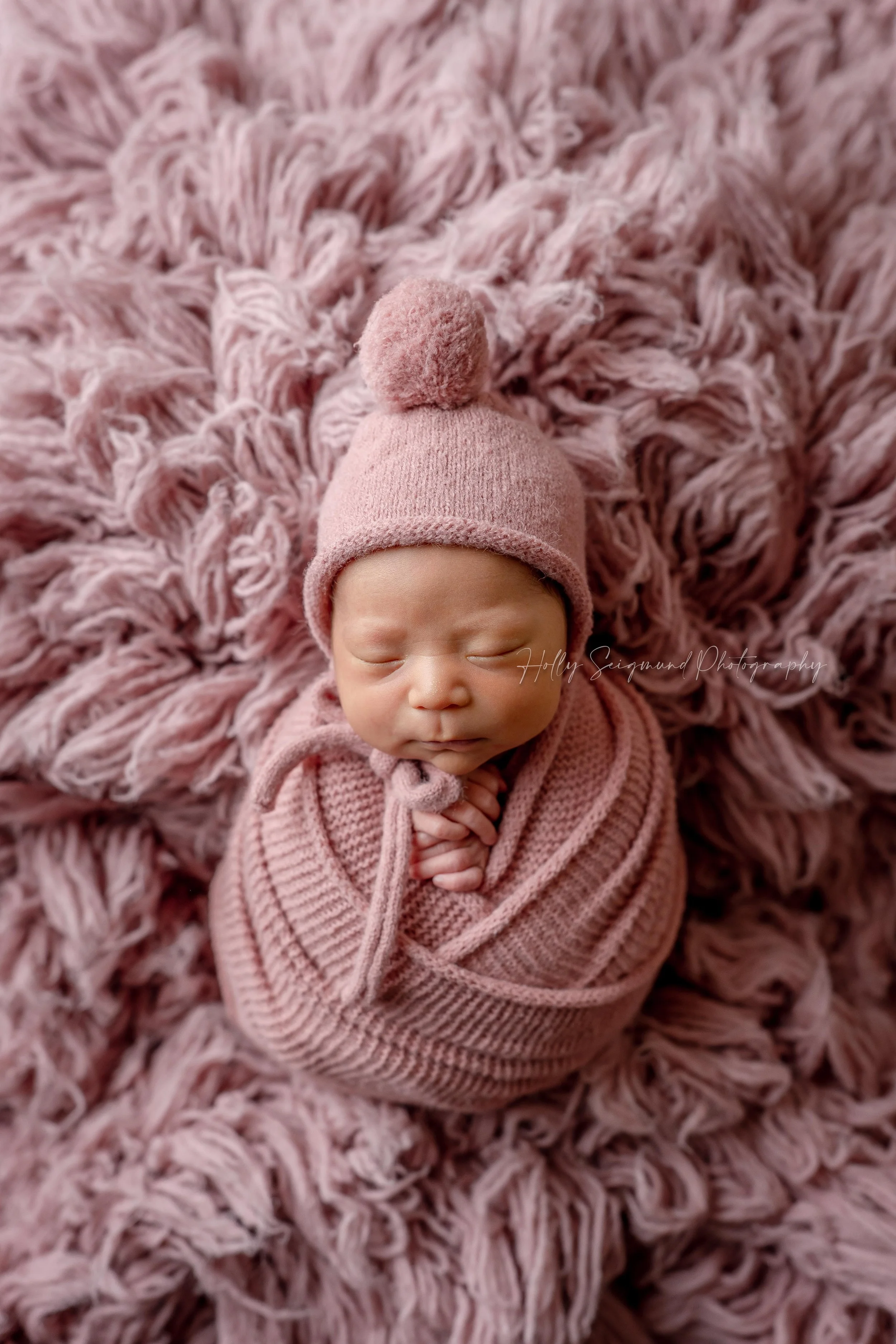 Baby girl wrapped in dusty rose on a dusty rose fluffy backdrop during a in-home studio session in Bastrop County