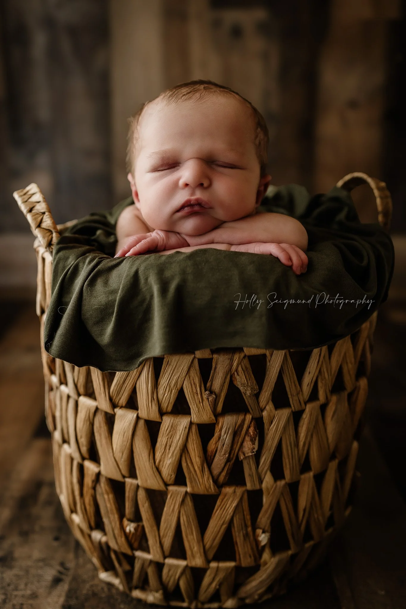 Newborn baby boy posed in a basket on a wood floor and wood backdrop in Lee County Texas