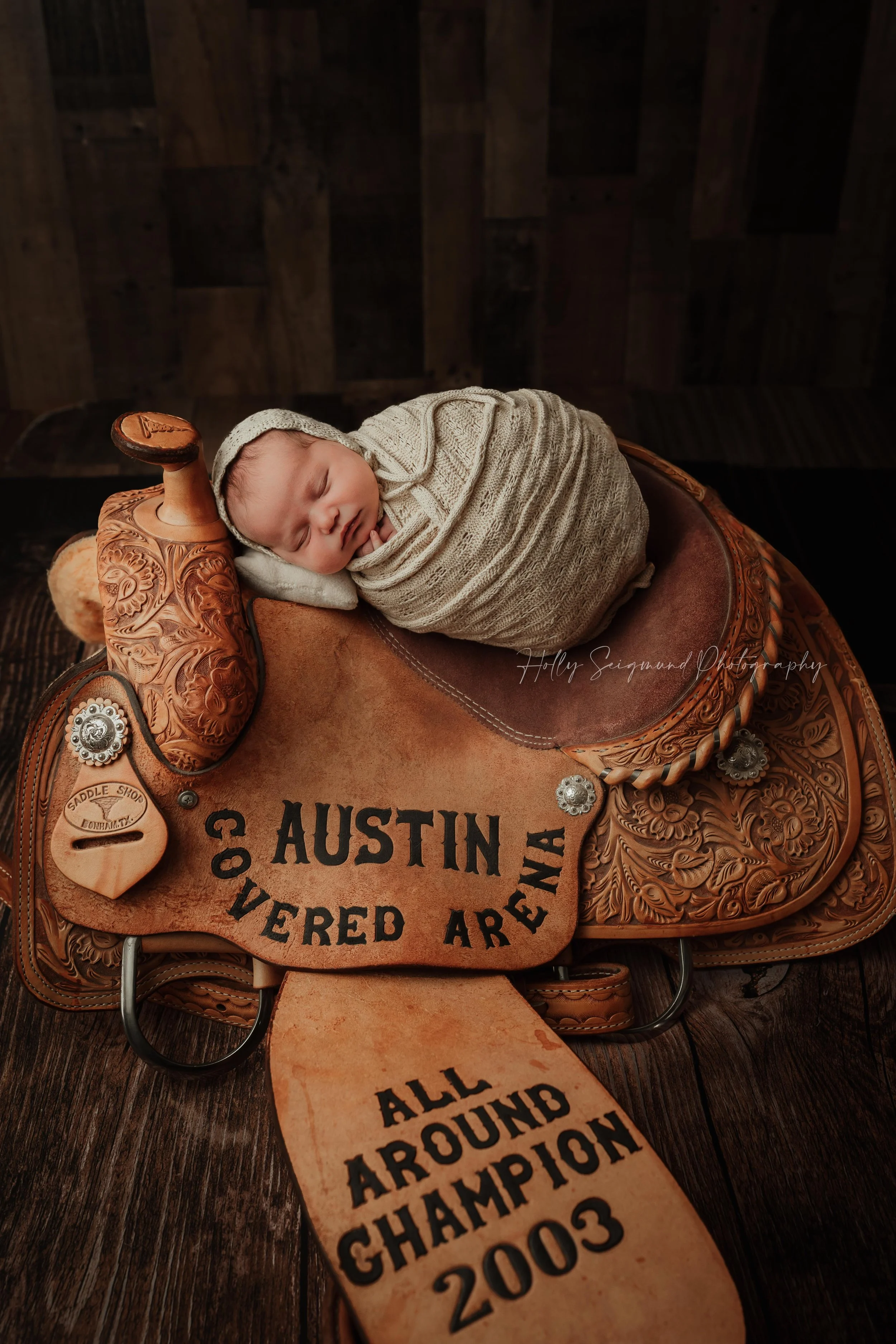 Newborn baby girl posed on her dad's horse saddle during her studio newborn session in Lexington, Texas