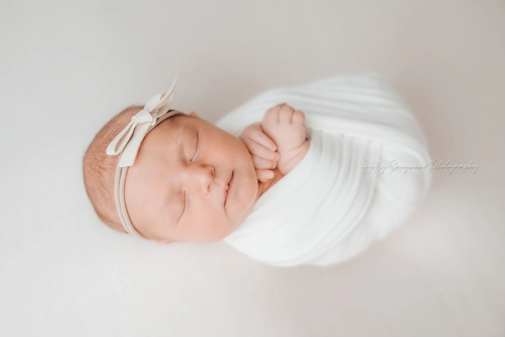 78947 newborn wrapped in white with a bow on a white backdrop