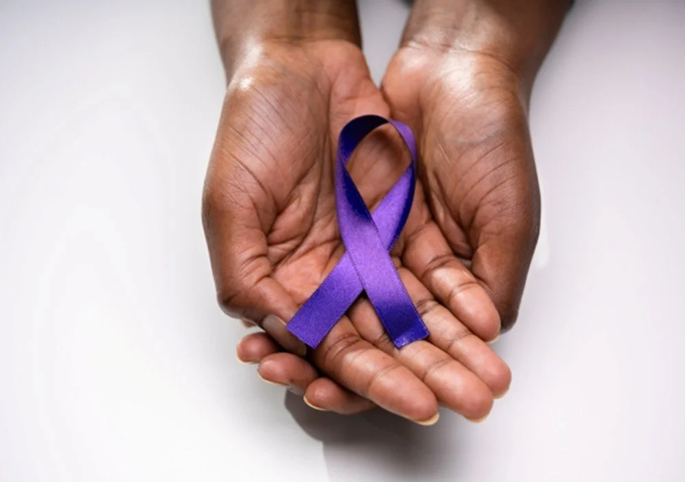 A hand holding a purple awareness ribbon in the shape of a loop.