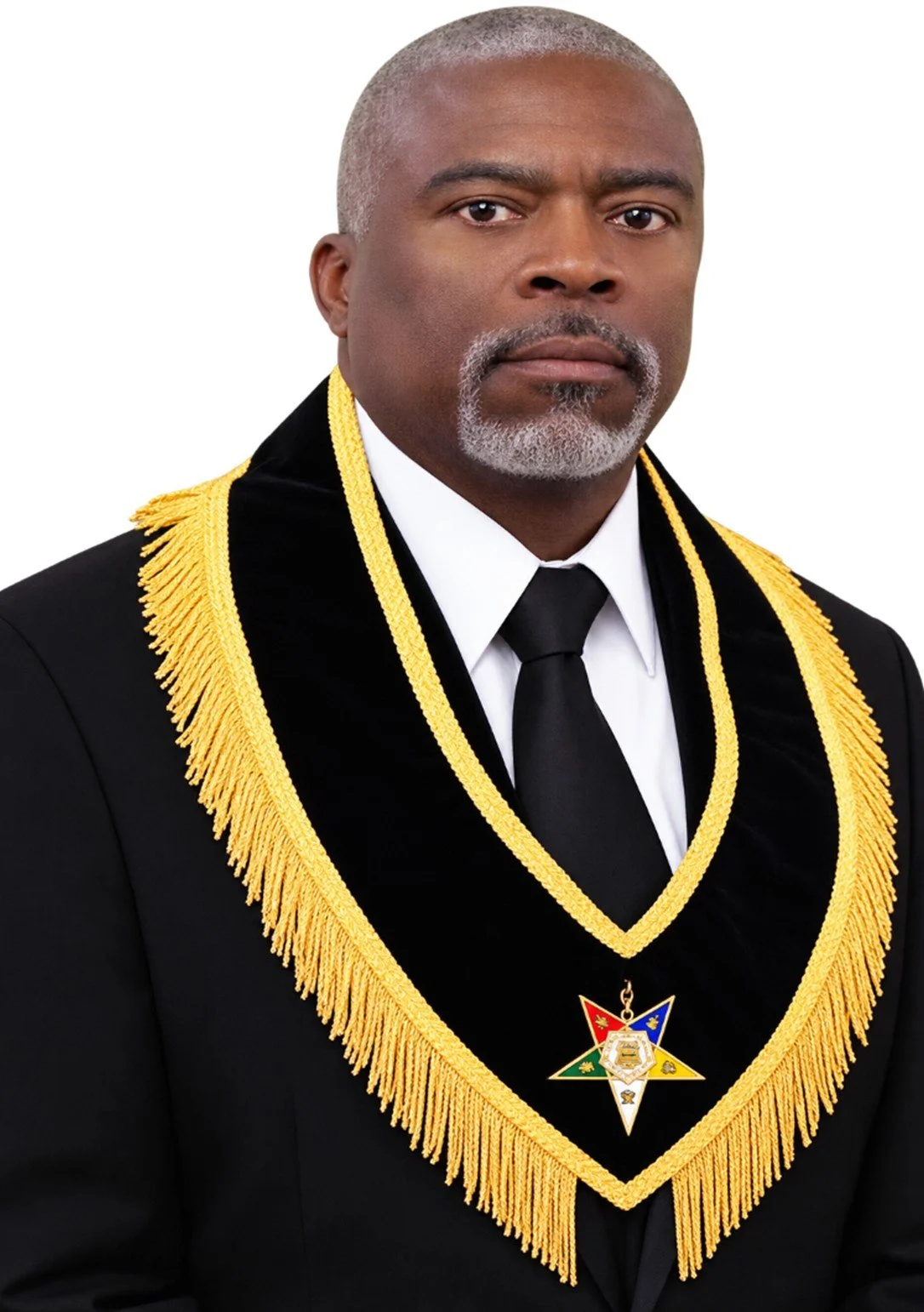 A man in a formal suit with a royal blue sash and gold fringe, standing in front of a colorful, abstract background.