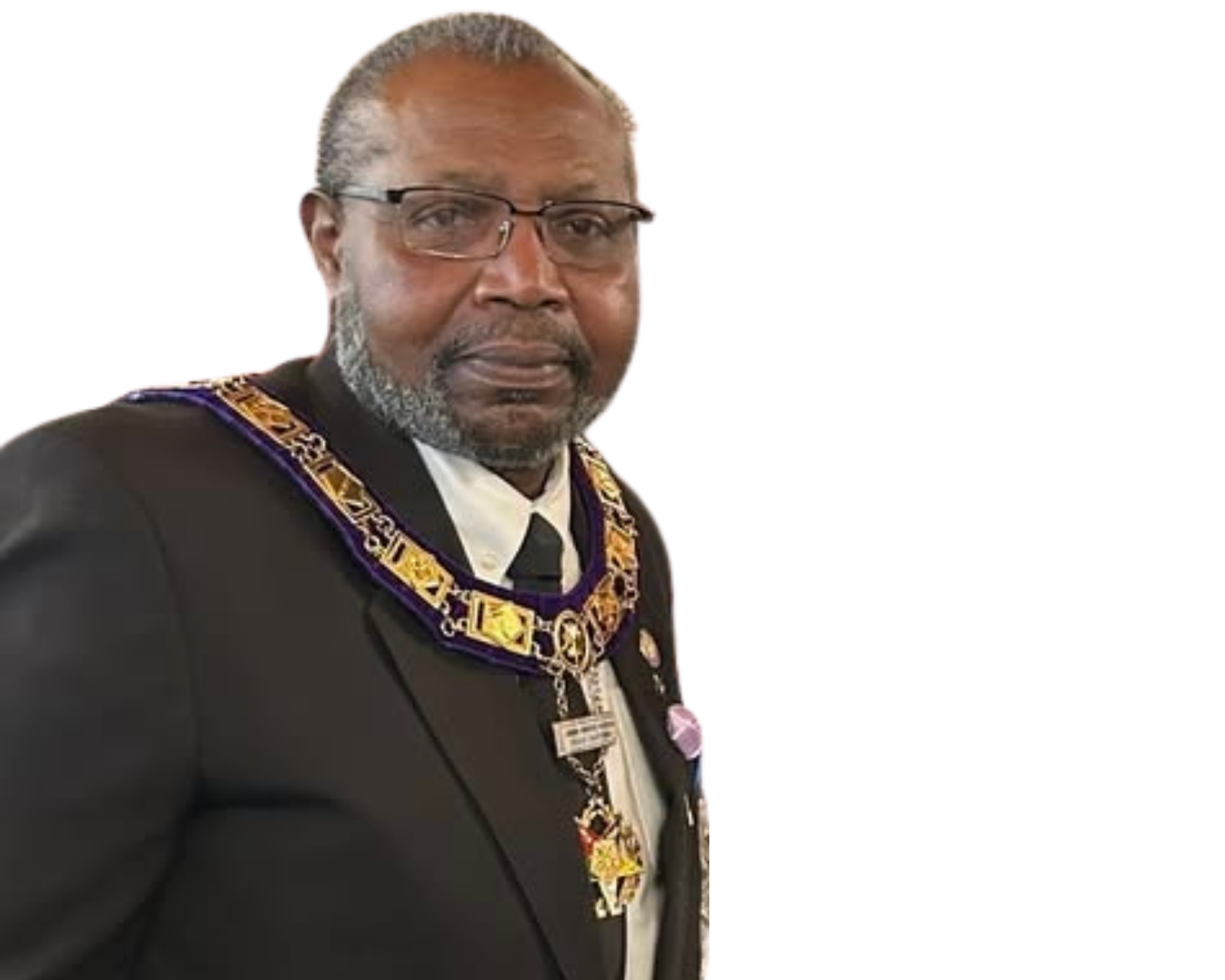 A man wearing glasses and a dark suit with ceremonial regalia, including a decorated chain and medals, standing against a neutral background.