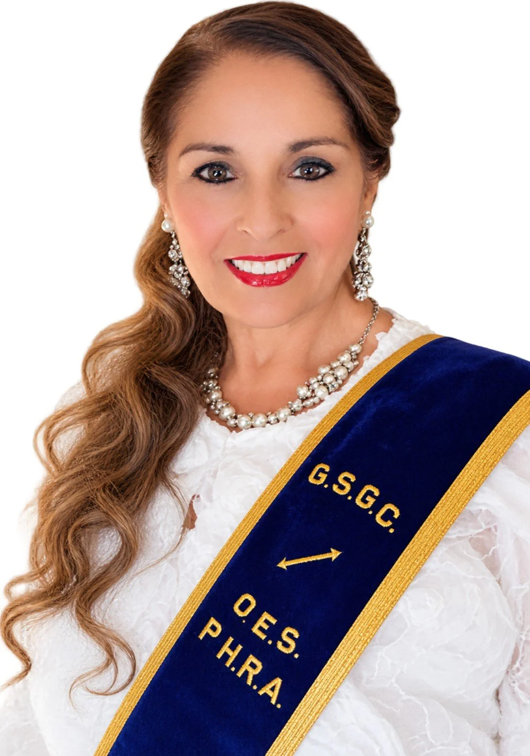 A woman with brown curly hair, wearing red lipstick, pearl earrings, and a white lace dress, standing against a colorful abstract background.