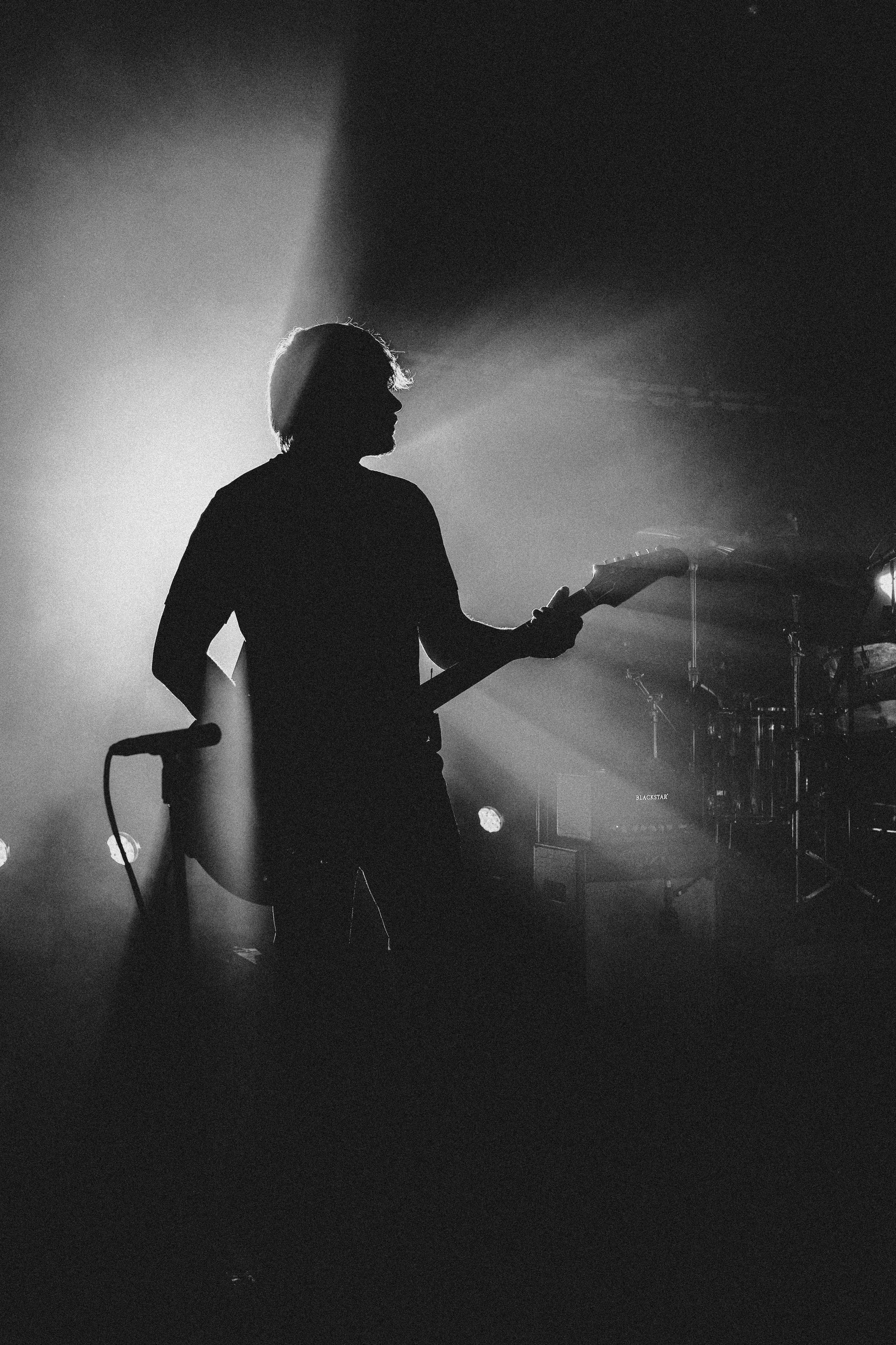 Silhouette of a person playing an electric guitar on stage, backlit with bright lights creating a dramatic atmosphere.