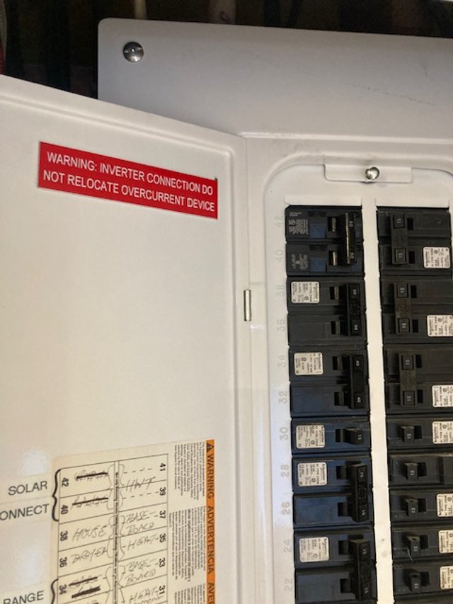 Open electrical panel with circuit breakers inside, warning labels on the door.