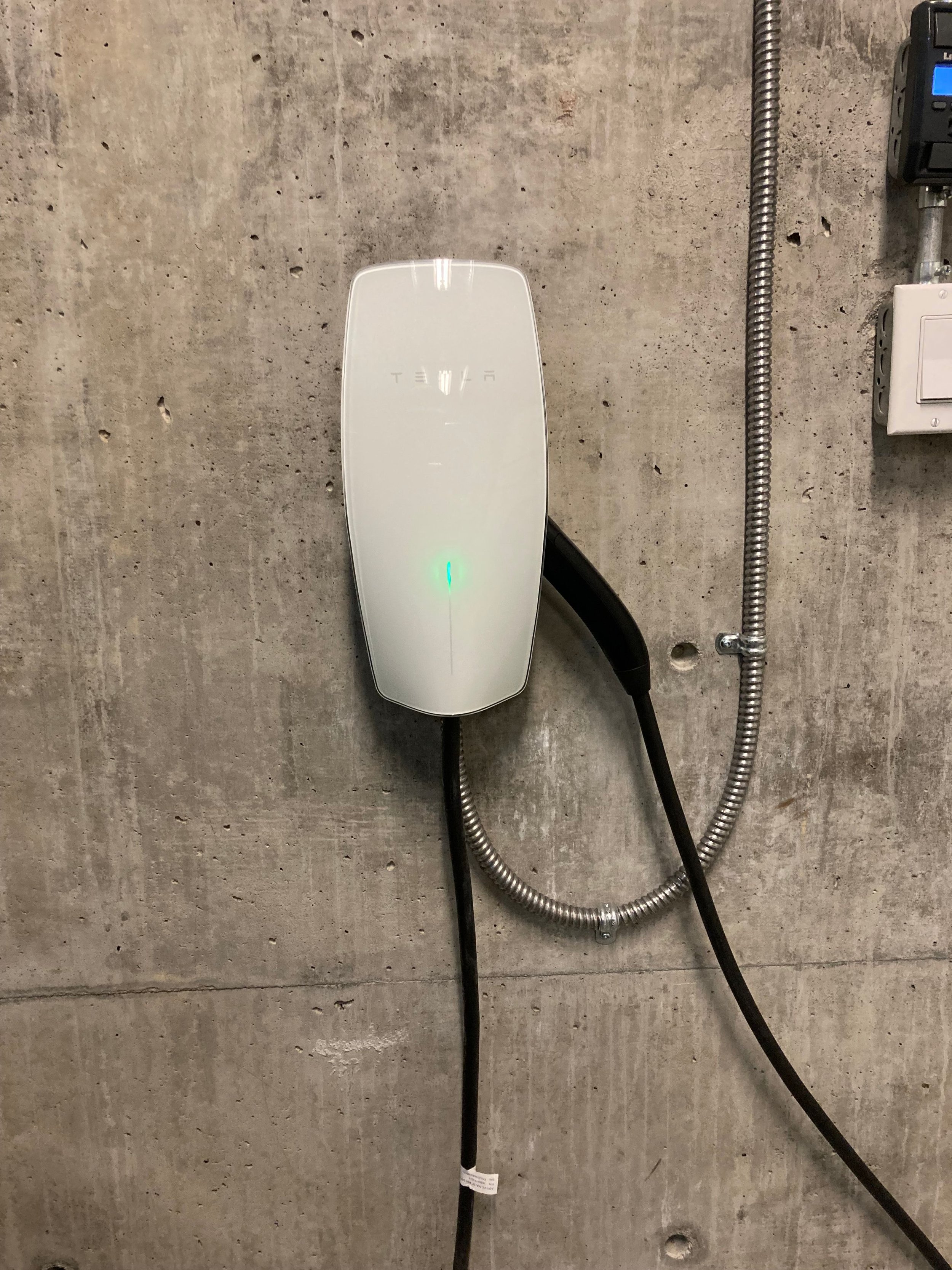 An electric charging station mounted on a concrete wall with black and gray cables connected to it.