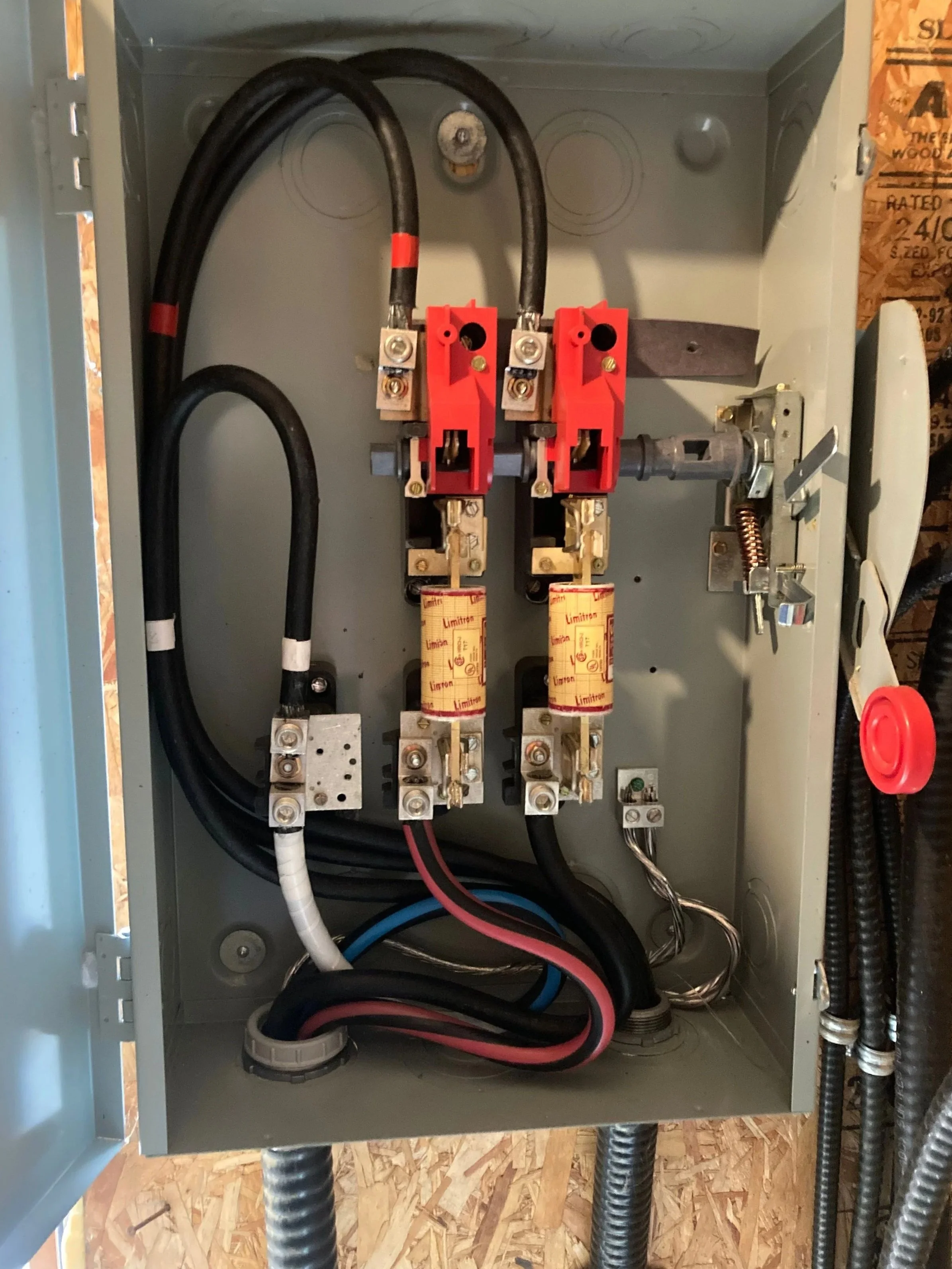 An electrical panel with wiring and components, including two circuit breakers with red levers and yellow labels, large black cables, and other smaller wires inside a metal box.