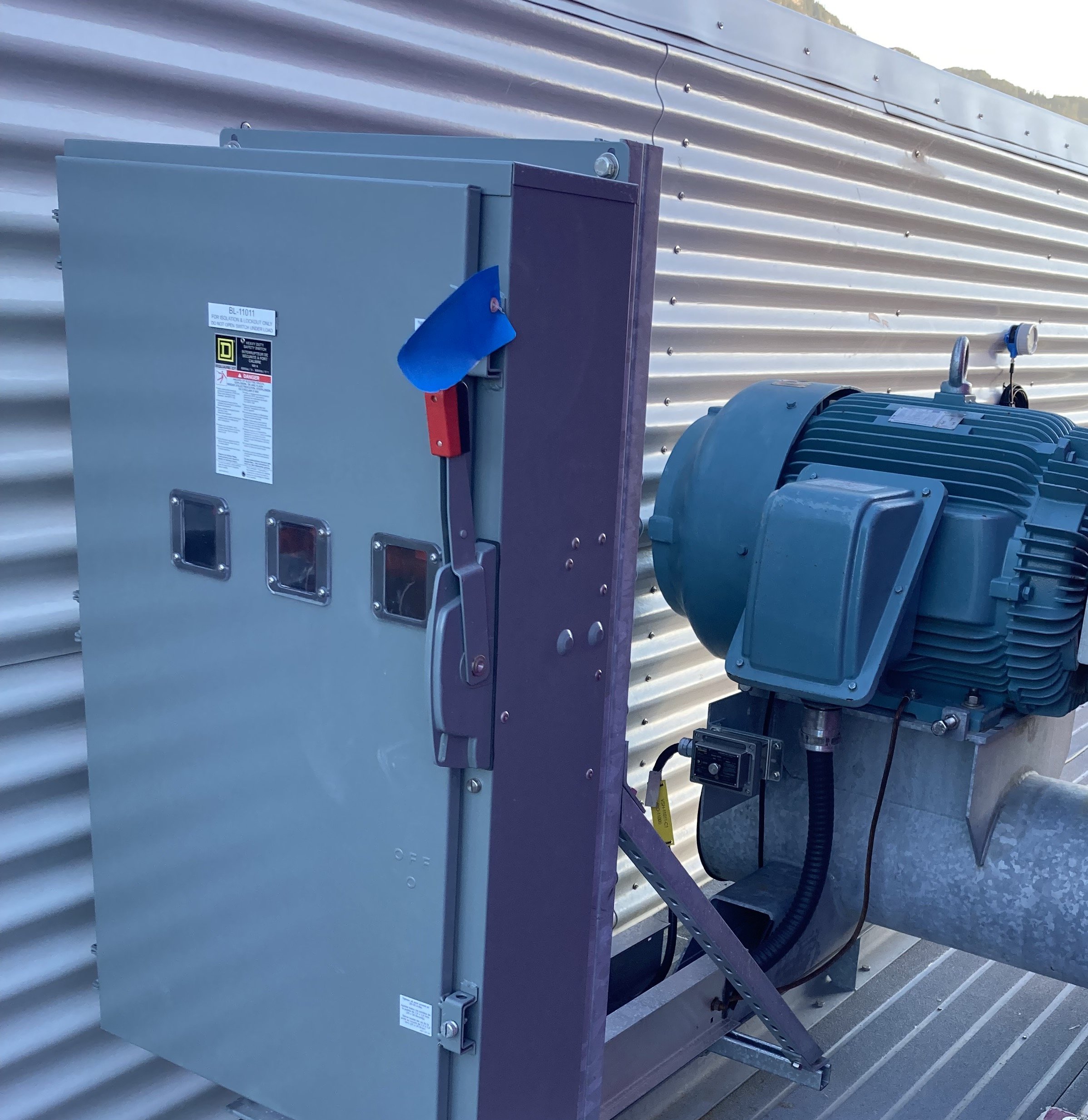 Electrical motor and control panel mounted outside a building with corrugated metal siding.