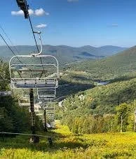 Empty ski lift chairs on a chairlift against a green mountain landscape and blue sky.