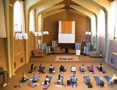 People practicing yoga on mats in a spacious room with large windows and wooden panels.