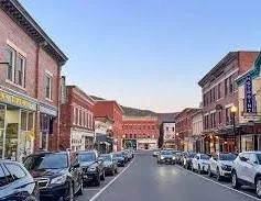 A small town Great Barrington main street with brick buildings, parked cars on either side, and a clear sky.