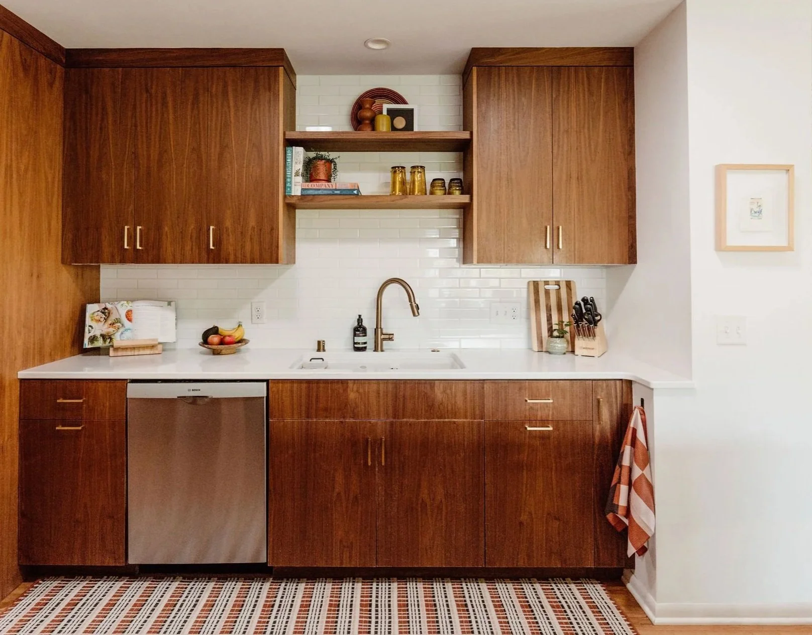 Kitchen design with contrasting elements: sleek walnut cabinetry, bright white wall tiles, and white countertops.