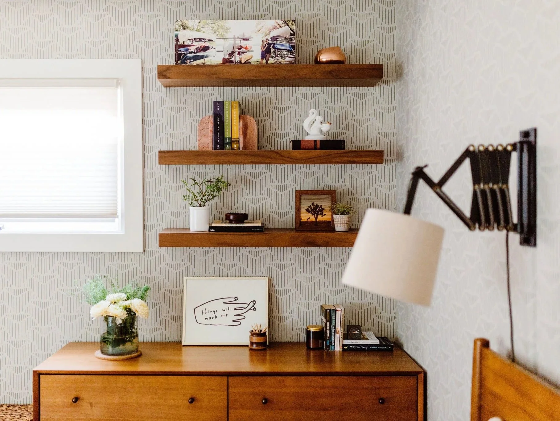 Interior of a room with a wooden sideboard, wall-mounted wooden shelves, decorative items, books, and a framed quote that says 'things will work out'.