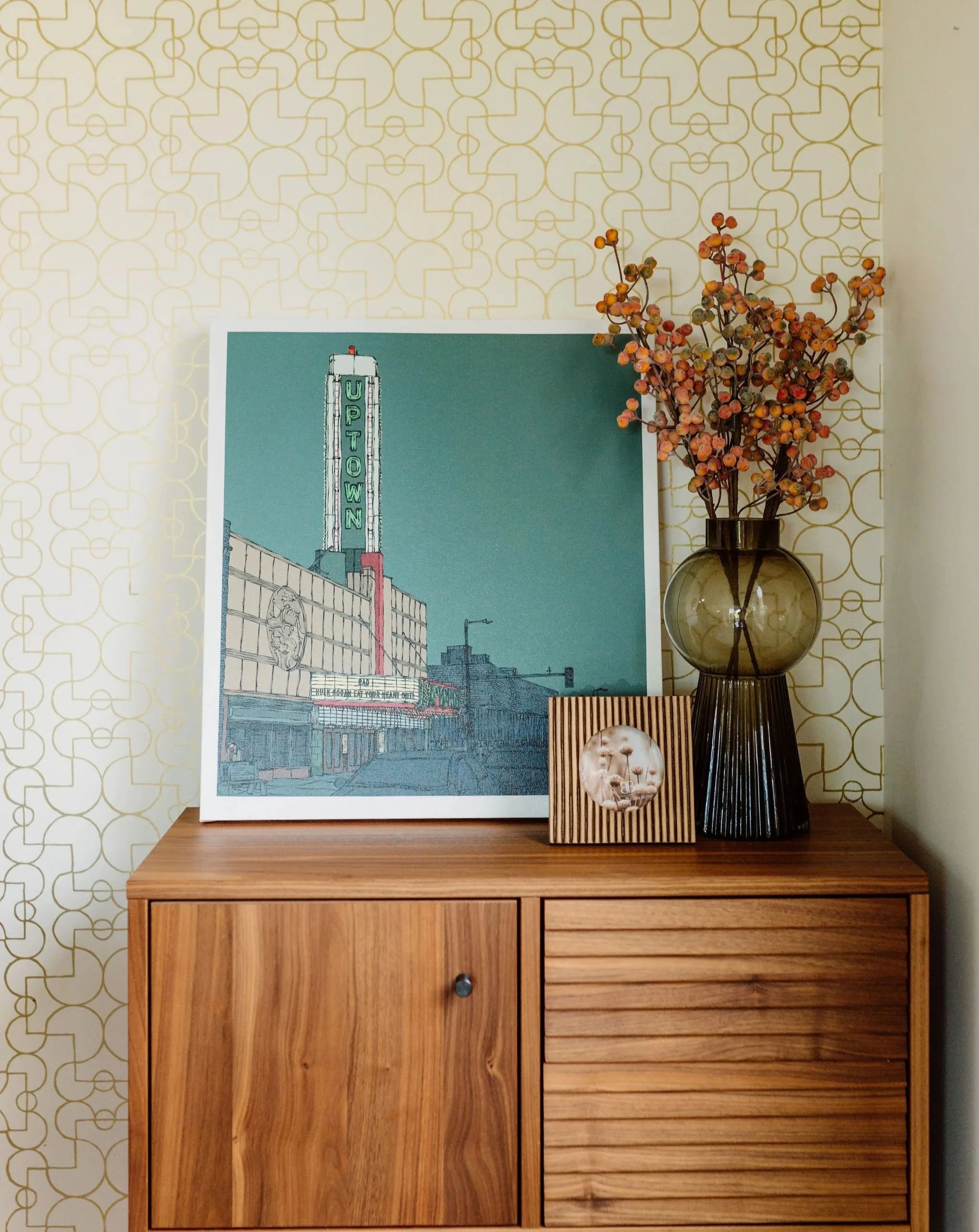Inviting dining room corner with a small buffet for storage, styled with custom local art, and a wallpaper backdrop.