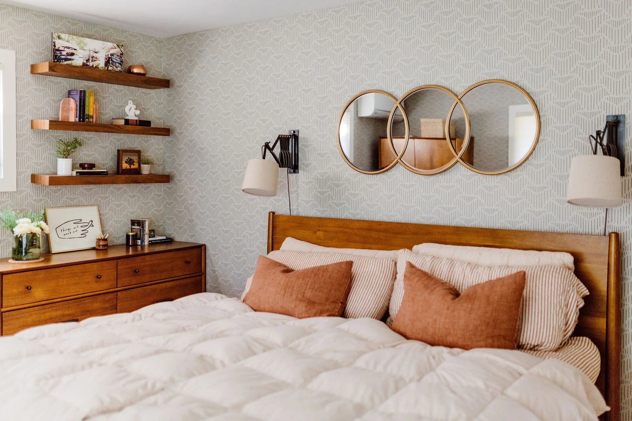 Symmetrical, cozy neutral bedroom with pattern wallpaper, plush bedding, and warm wood accents creating a serene retreat.