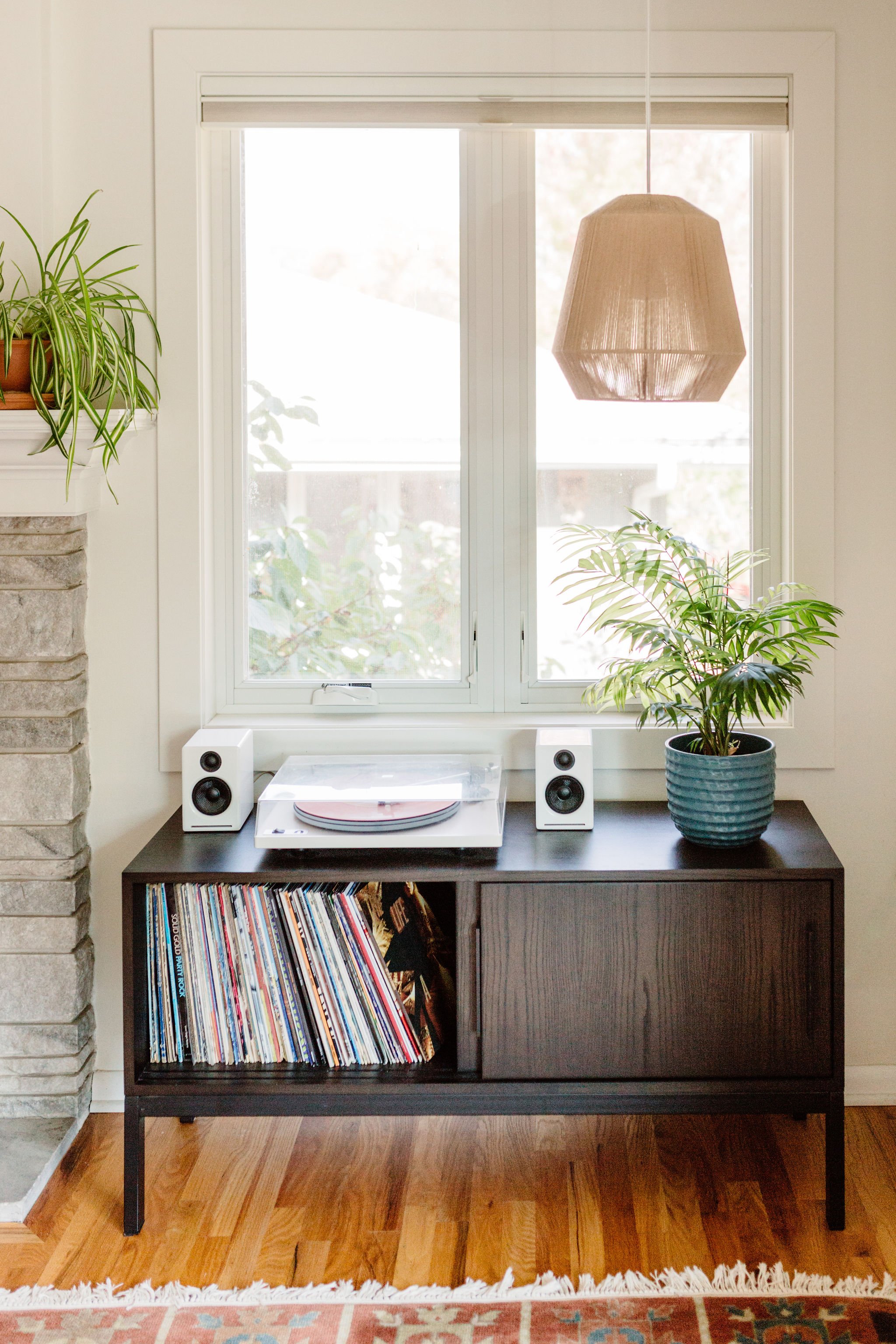 Cozy music corner with a record player on a modern wooden cabinet, surrounded by plants. 