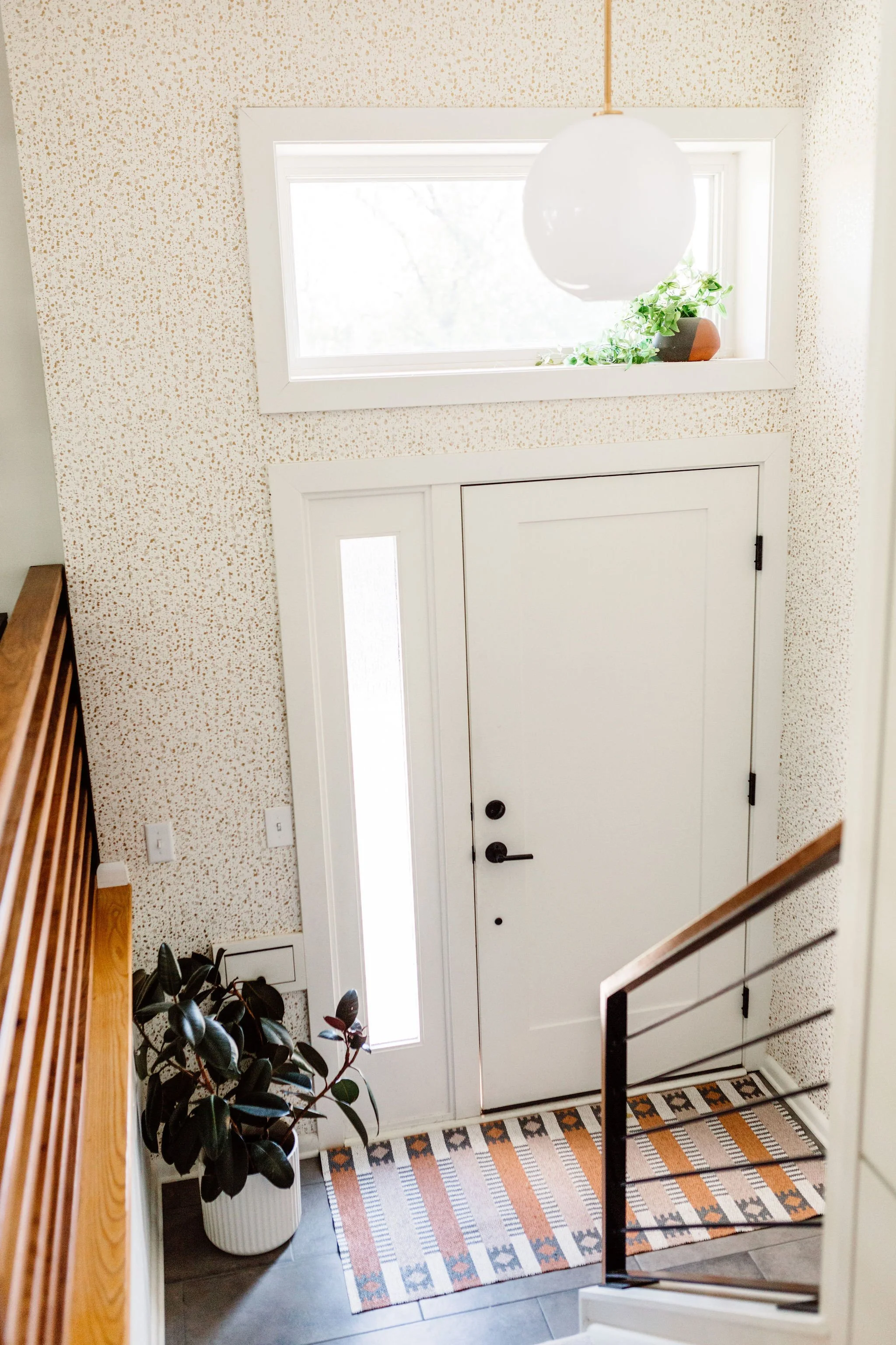 Minimalist modern entryway with a neutral color palette, subtle-patterned wallpaper, and a playful Scandinavian-style rug.