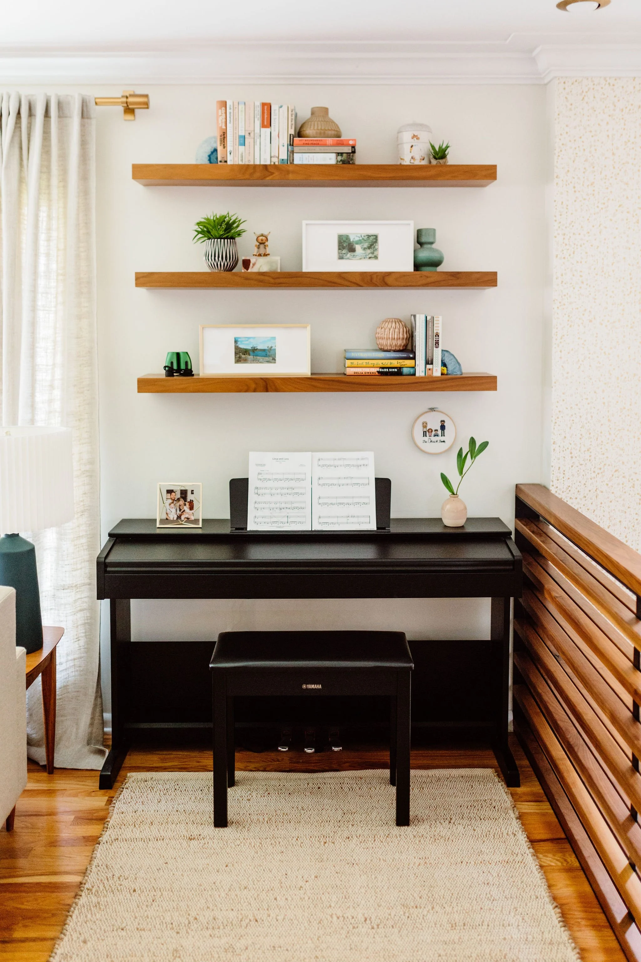 Utilizing vertical space with floating wall shelves above a piano, optimizing a challenging layout. 