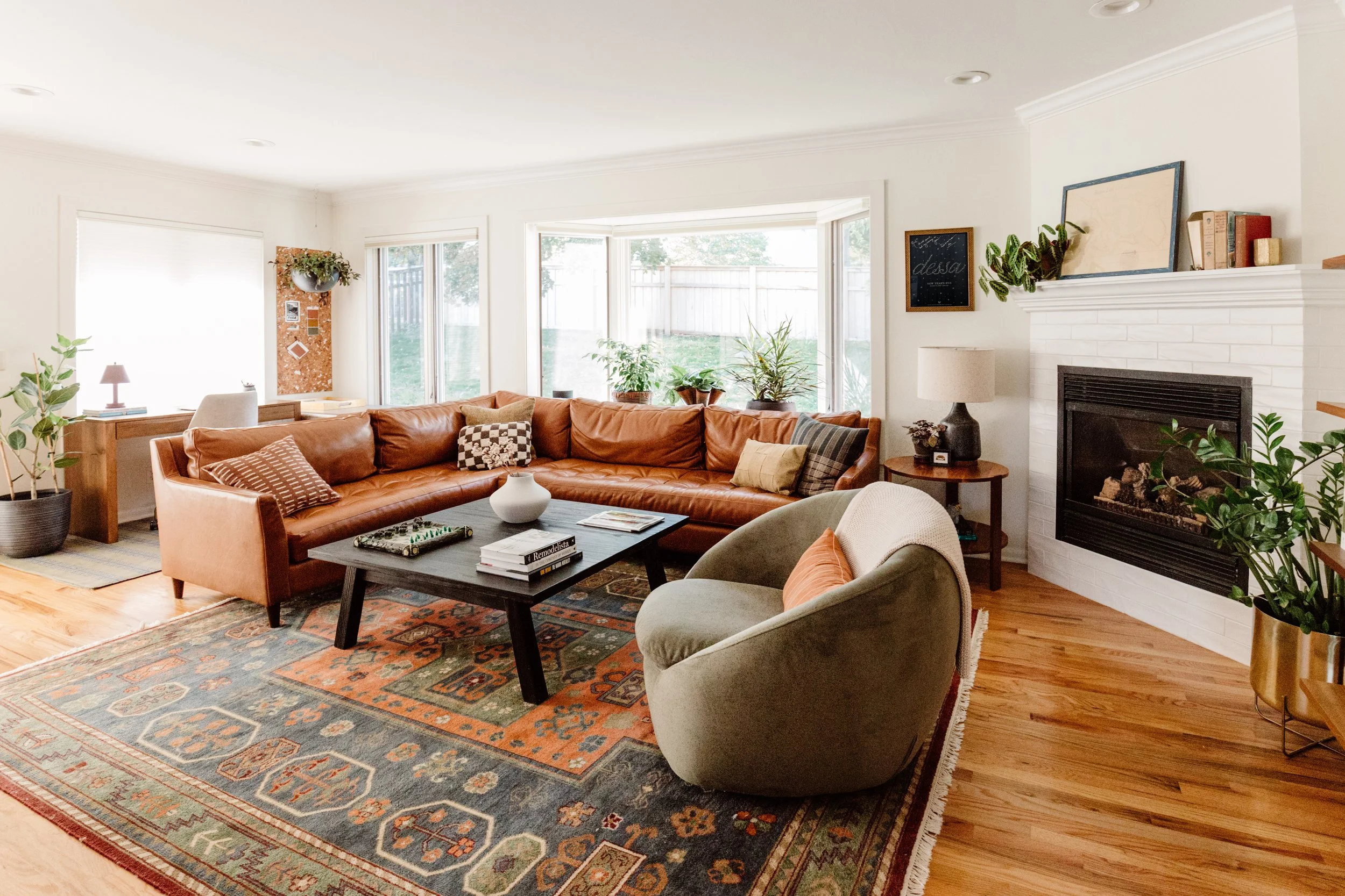 Large family room with warm neutral colors, a brown leather sectional, and abundant natural light from wide windows.