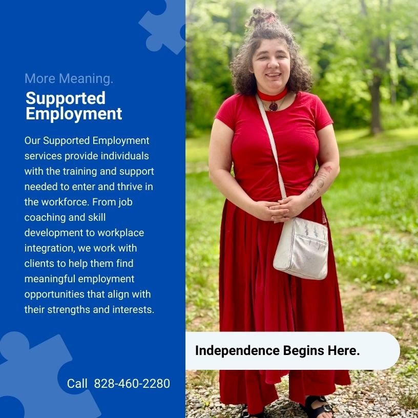 A woman in a red dress and black sandals is standing outdoors in a park with green trees in the background. She has curly hair, a necklace, and carries a small beige bag.