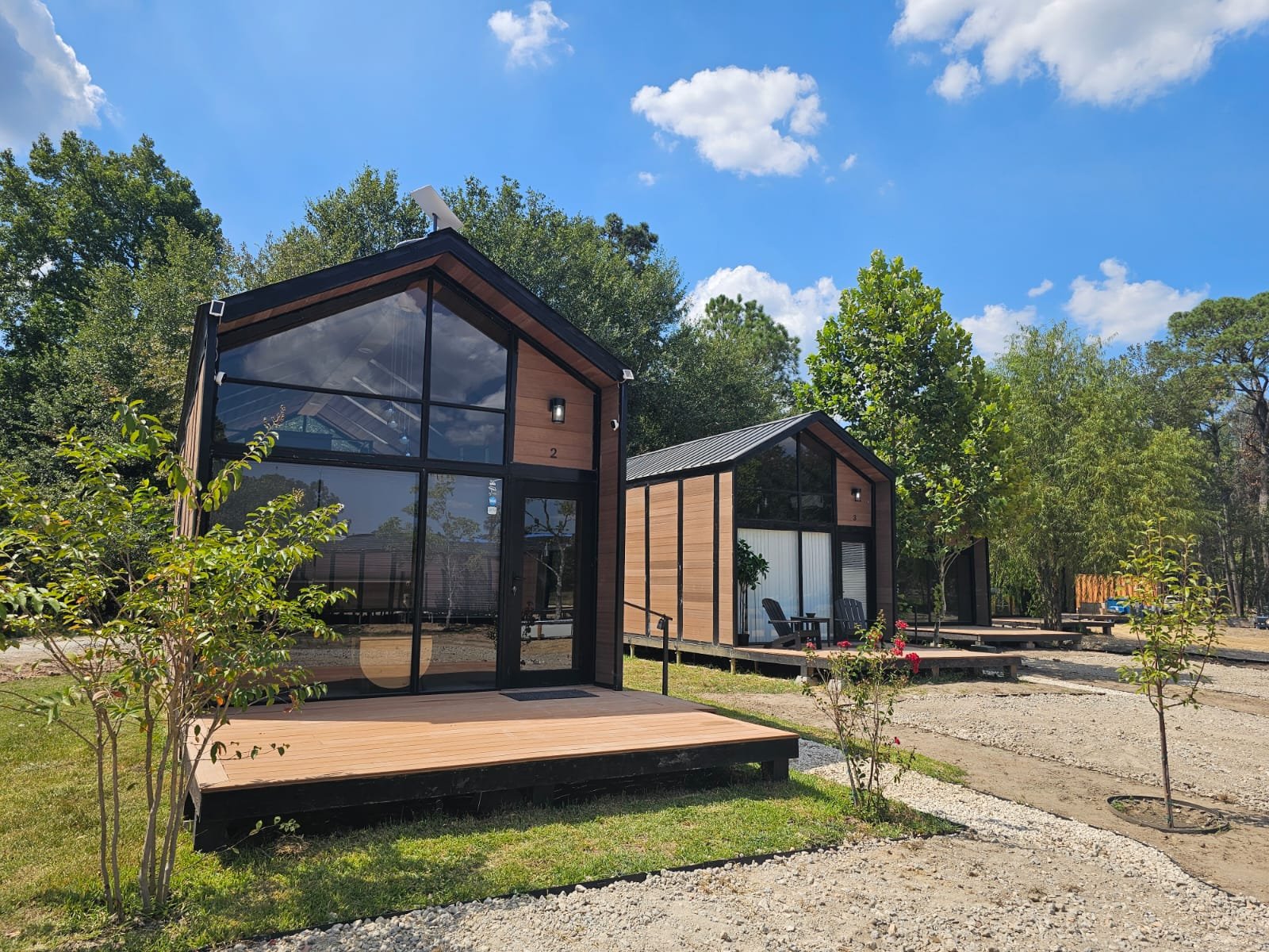 Modern NeoVita tiny houses with large glass windows and wood siding in a natural setting under a blue sky.
