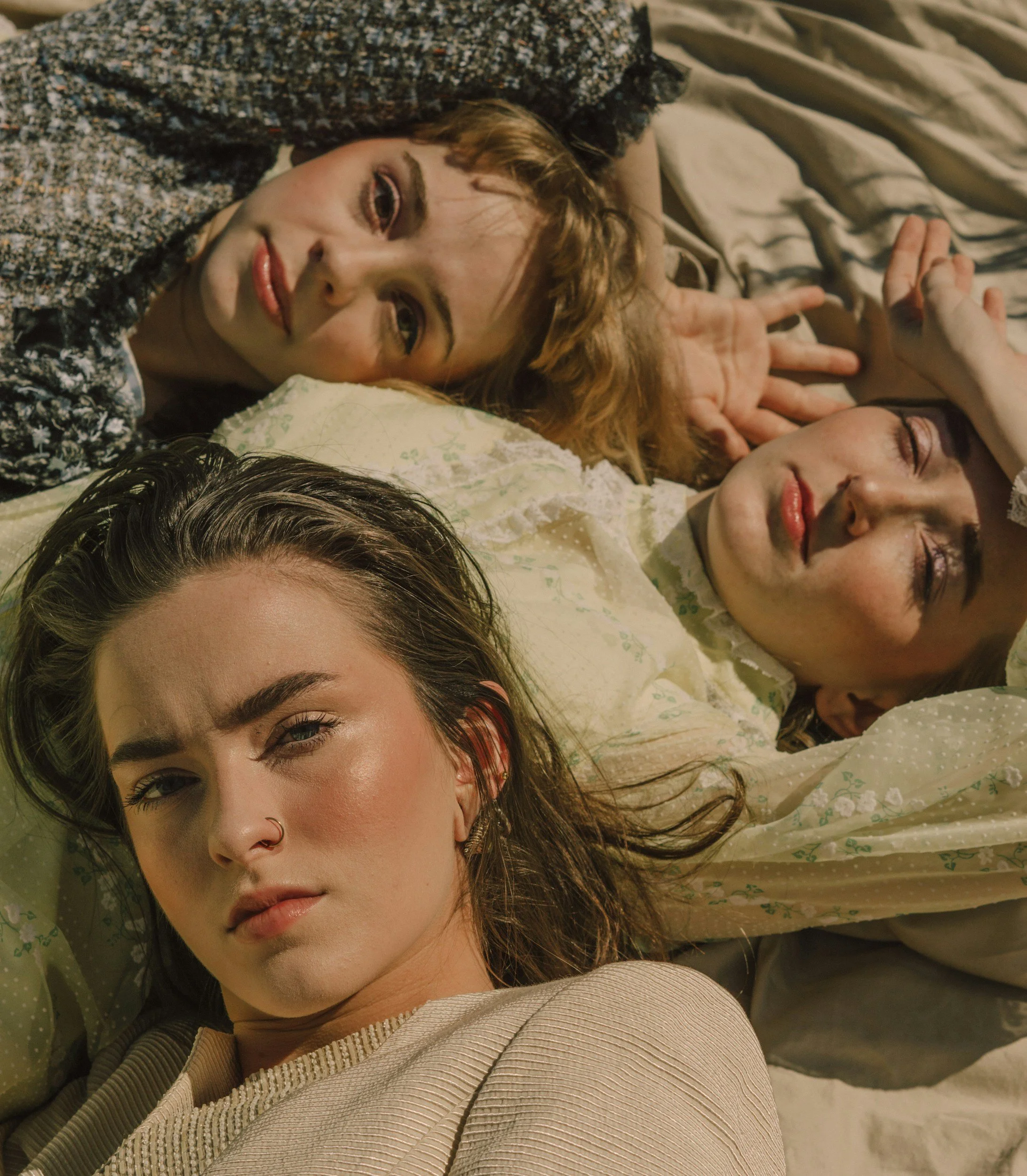 Close-up of a woman with brown hair and piercing blue eyes lying down on a bed, surrounded by others partially visible, with her face near the camera.