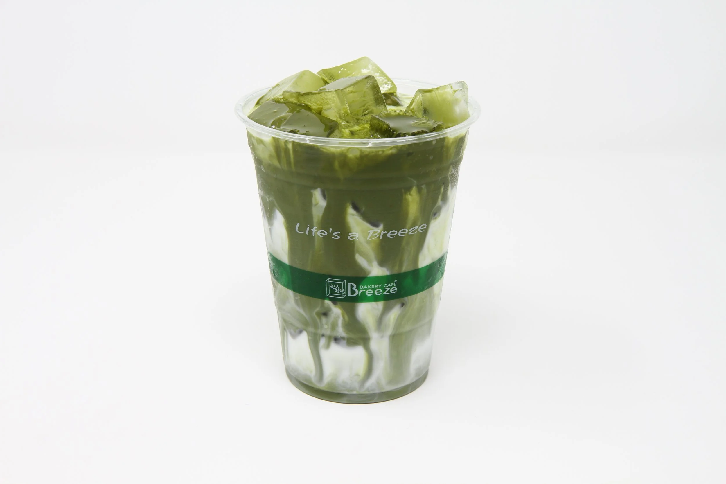 Iced matcha latte in clear plastic cup, matcha sauce is dripping from top to bottom as it mixes with the milk.